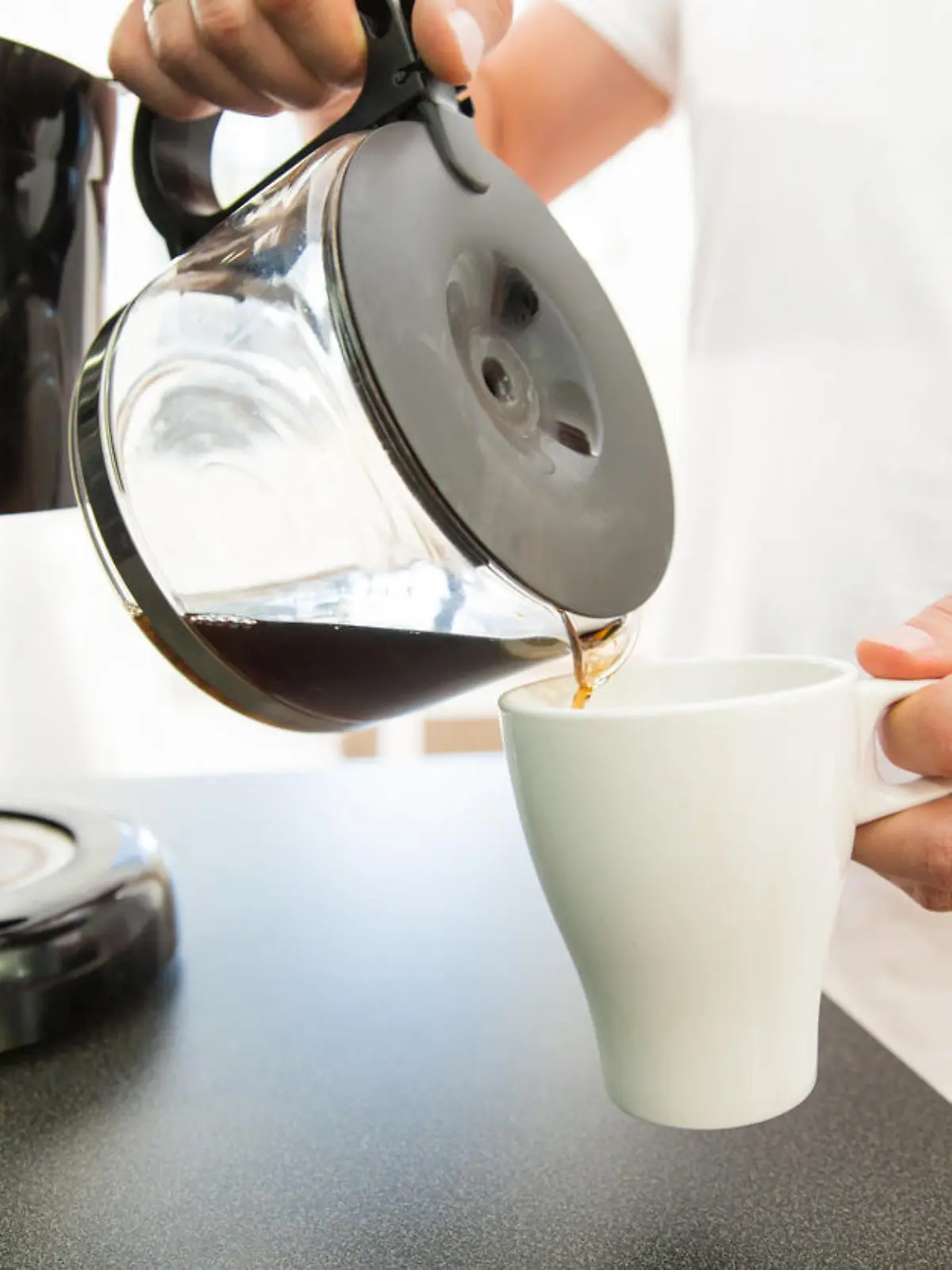 Ein Mann gießt sich am Morgen eine Tasse Kaffee aus einer Filtermaschine ein.