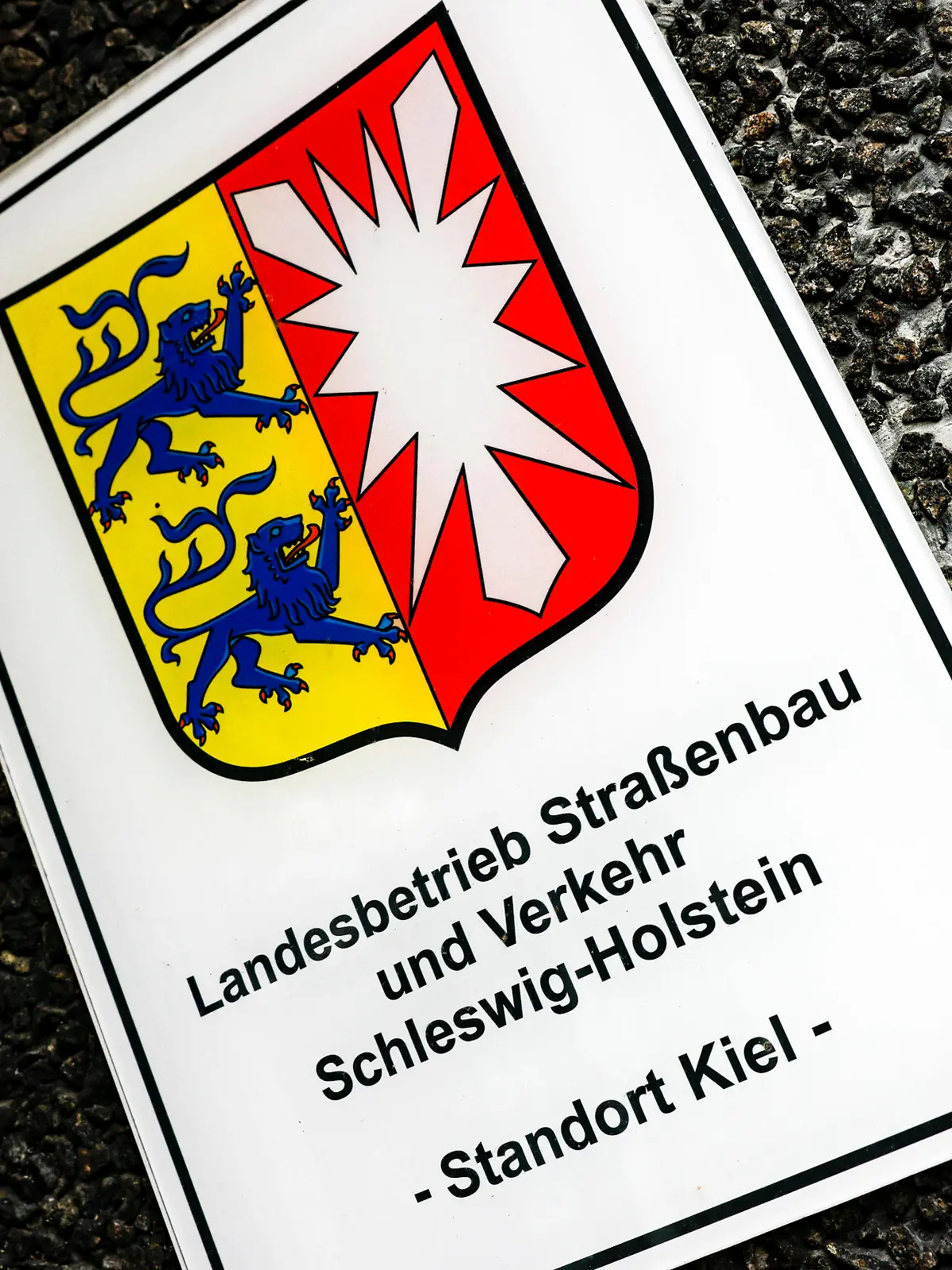 ARCHIV - 01.02.2023, Schleswig-Holstein, Kiel: Ein Hinweisschild auf den Sitz vom Landesbetrieb Straßenbau und Verkehr hängt am Eingang zur Hauptstelle. Die schleswig-holsteinische FDP kritisiert die geplante Umbenennung des Landesbetriebs.      (zu dpa «210 000 Euro für die Streichung eines Wortes») Foto: Axel Heimken/dpa +++ dpa-Bildfunk +++