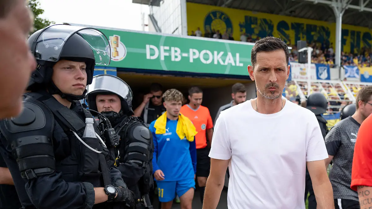 13.08.2023, Sachsen, Leipzig: Fußball: DFB-Pokal, Lok Leipzig - Eintracht Frankfurt, 1. Runde, Bruno Plache Stadion. Nach einer Spielunterbrechung kommen die Mannschaften, hier Frankfurts Trainer Dino Toppmöller (2.v.r.) unter Polizeischutz wieder ins Stadion. Foto: Hendrik Schmidt/dpa - WICHTIGER HINWEIS: Gemäß den Vorgaben der DFL Deutsche Fußball Liga bzw. des DFB Deutscher Fußball-Bund ist es untersagt, in dem Stadion und/oder vom Spiel angefertigte Fotoaufnahmen in Form von Sequenzbildern und/oder videoähnlichen Fotostrecken zu verwerten bzw. verwerten zu lassen. +++ dpa-Bildfunk +++