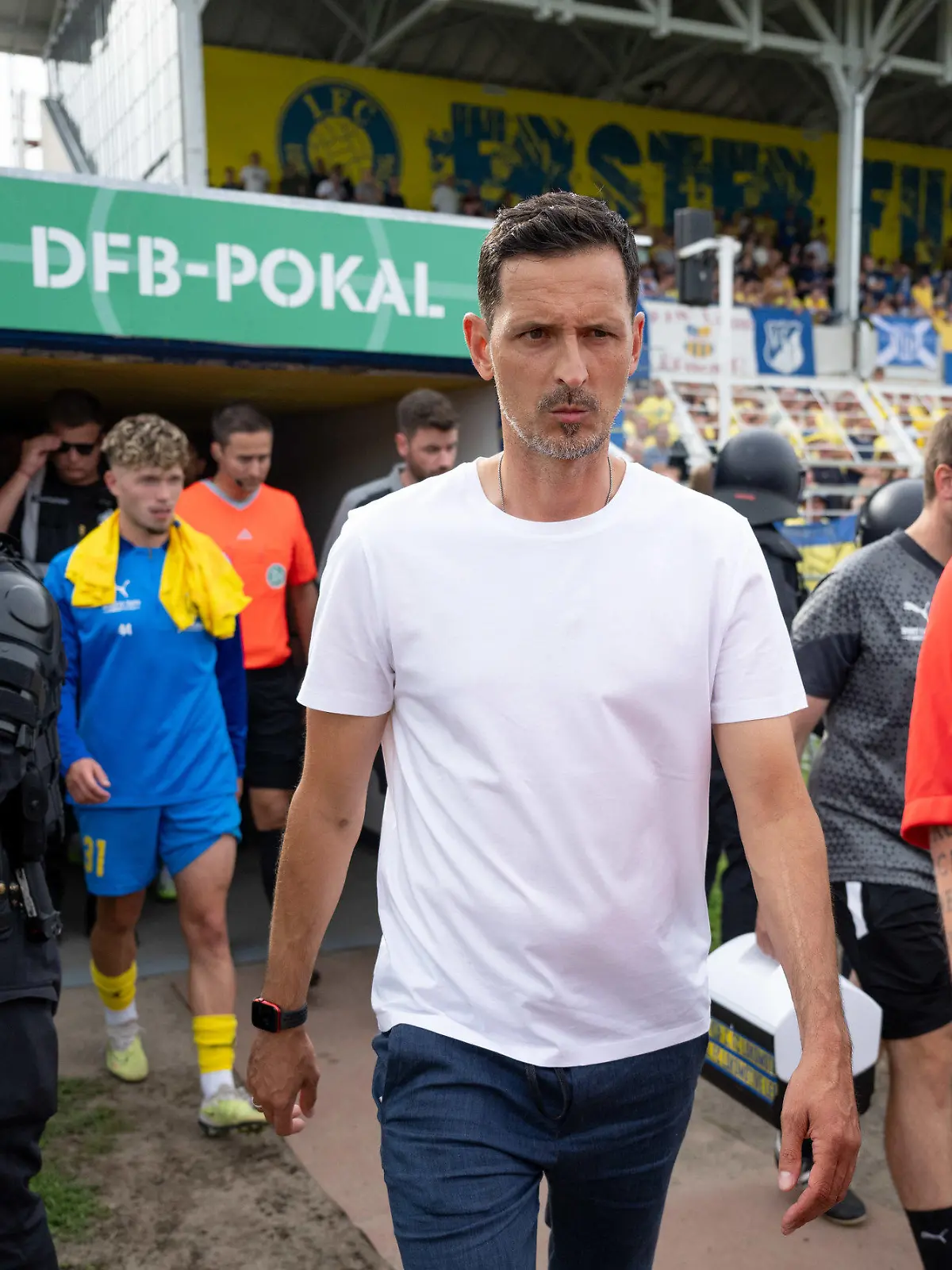 13.08.2023, Sachsen, Leipzig: Fußball: DFB-Pokal, Lok Leipzig - Eintracht Frankfurt, 1. Runde, Bruno Plache Stadion. Nach einer Spielunterbrechung kommen die Mannschaften, hier Frankfurts Trainer Dino Toppmöller (2.v.r.) unter Polizeischutz wieder ins Stadion. Foto: Hendrik Schmidt/dpa - WICHTIGER HINWEIS: Gemäß den Vorgaben der DFL Deutsche Fußball Liga bzw. des DFB Deutscher Fußball-Bund ist es untersagt, in dem Stadion und/oder vom Spiel angefertigte Fotoaufnahmen in Form von Sequenzbildern und/oder videoähnlichen Fotostrecken zu verwerten bzw. verwerten zu lassen. +++ dpa-Bildfunk +++