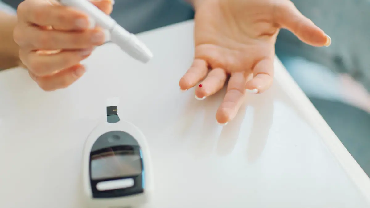 Mature woman doing blood sugar test at home in a living room. Selective focus to her finger with blood.