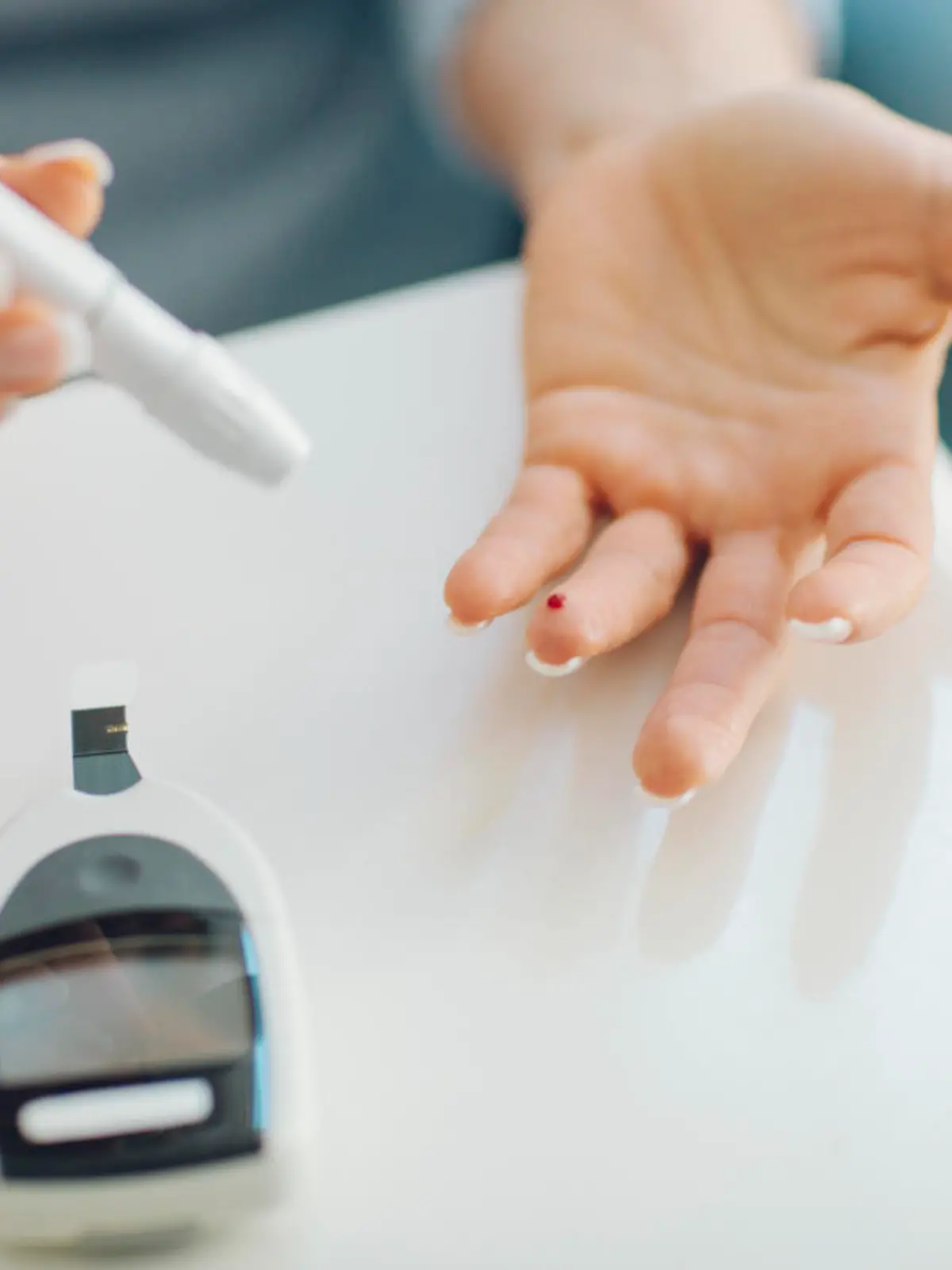 Mature woman doing blood sugar test at home in a living room. Selective focus to her finger with blood.