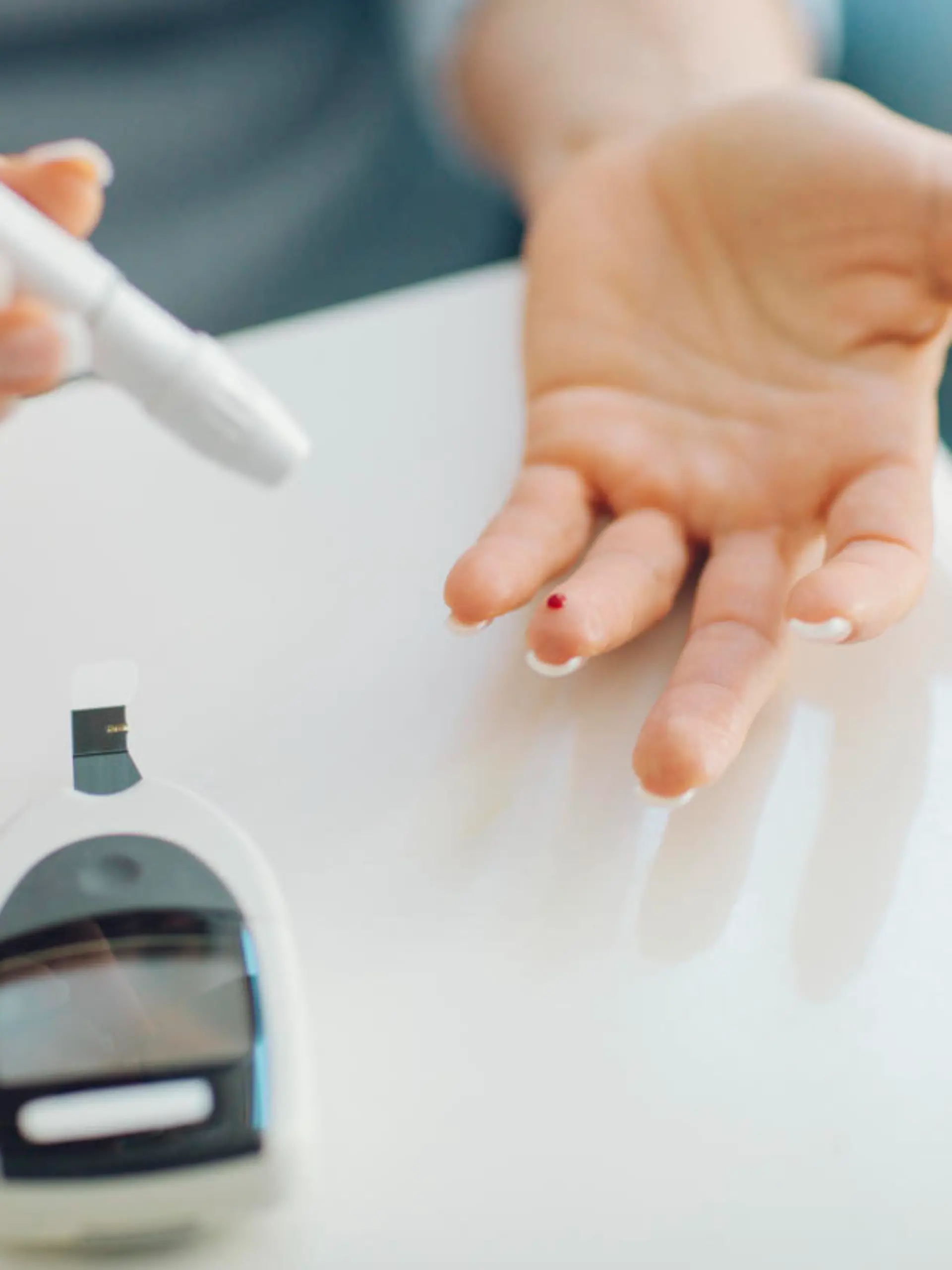 Mature woman doing blood sugar test at home in a living room. Selective focus to her finger with blood.