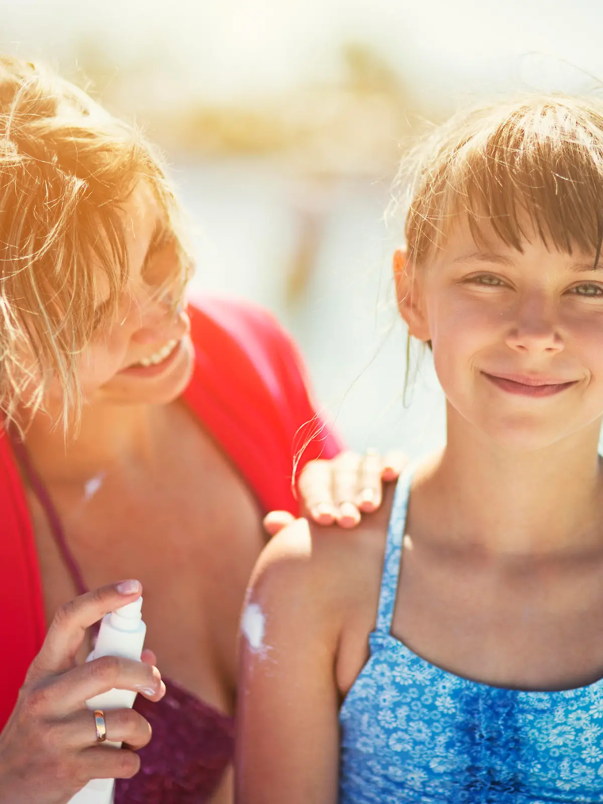 Mother and daughter on beach. Mother is applying sunscreen lotion on her daughter. The girl is aged 8. 