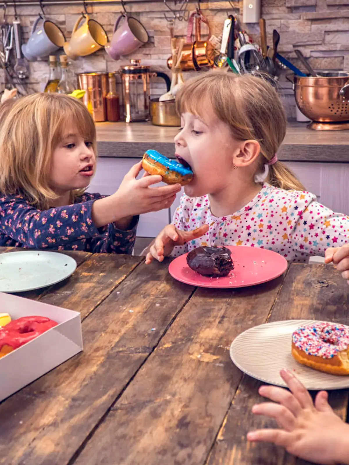 Cute little kids eating various donuts with colored icing and chocolate.