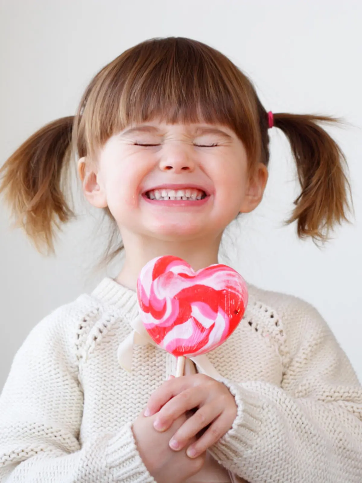 Ein kleines Mädchen hält sich grinsend einen Lolli vor den Mund.