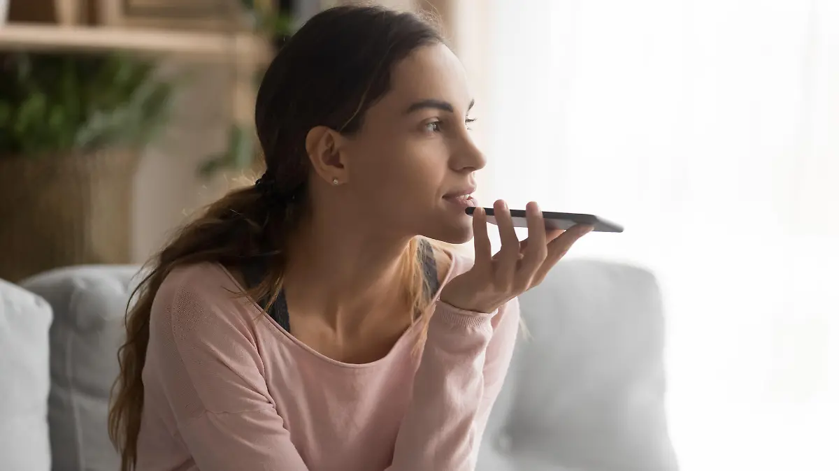 Woman sitting on couch holds phone talks on speakerphone with friend, makes voice recognition or request uses internet services through virtual assistant, record audio message, translator app concept