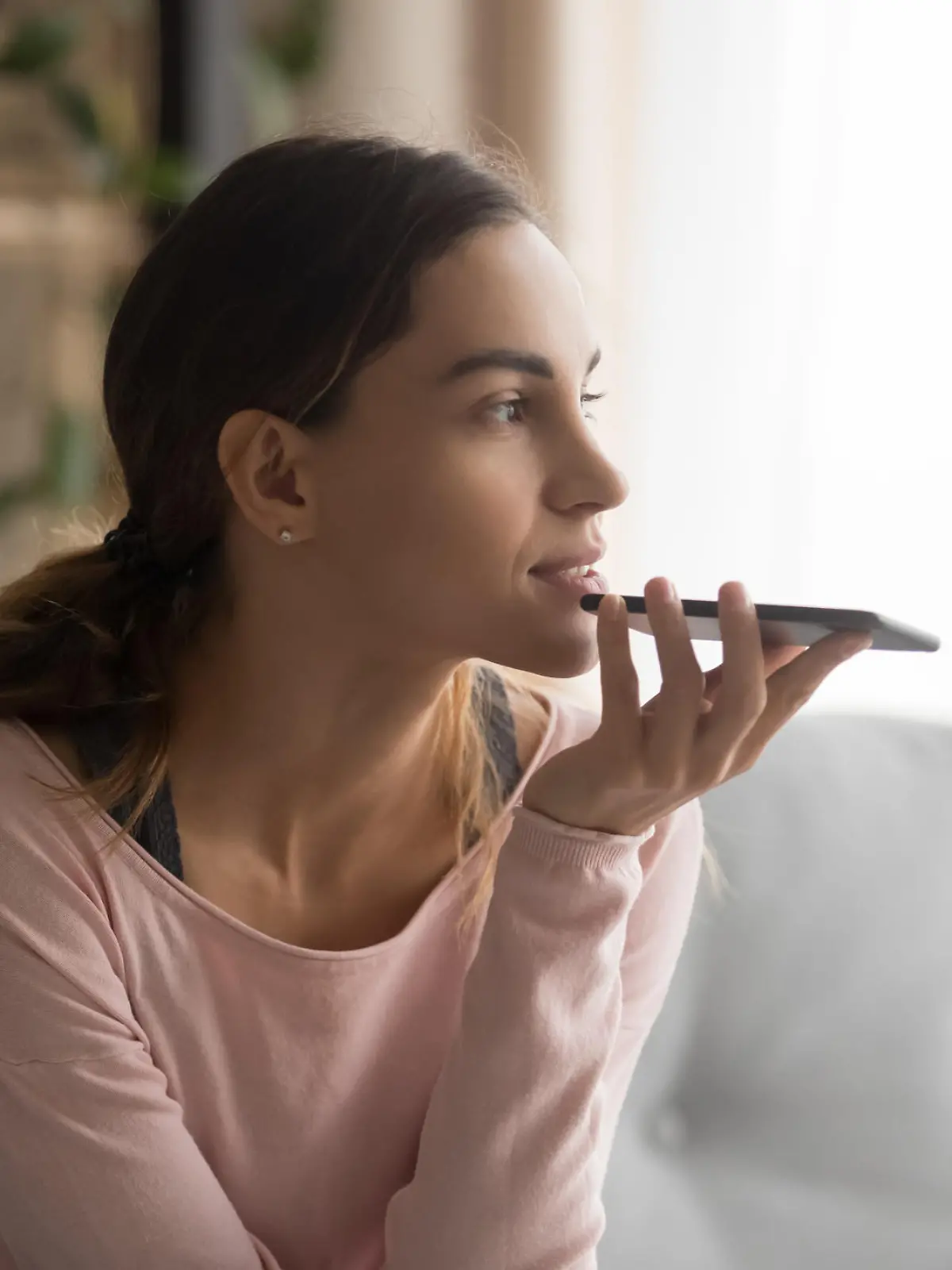 Woman sitting on couch holds phone talks on speakerphone with friend, makes voice recognition or request uses internet services through virtual assistant, record audio message, translator app concept