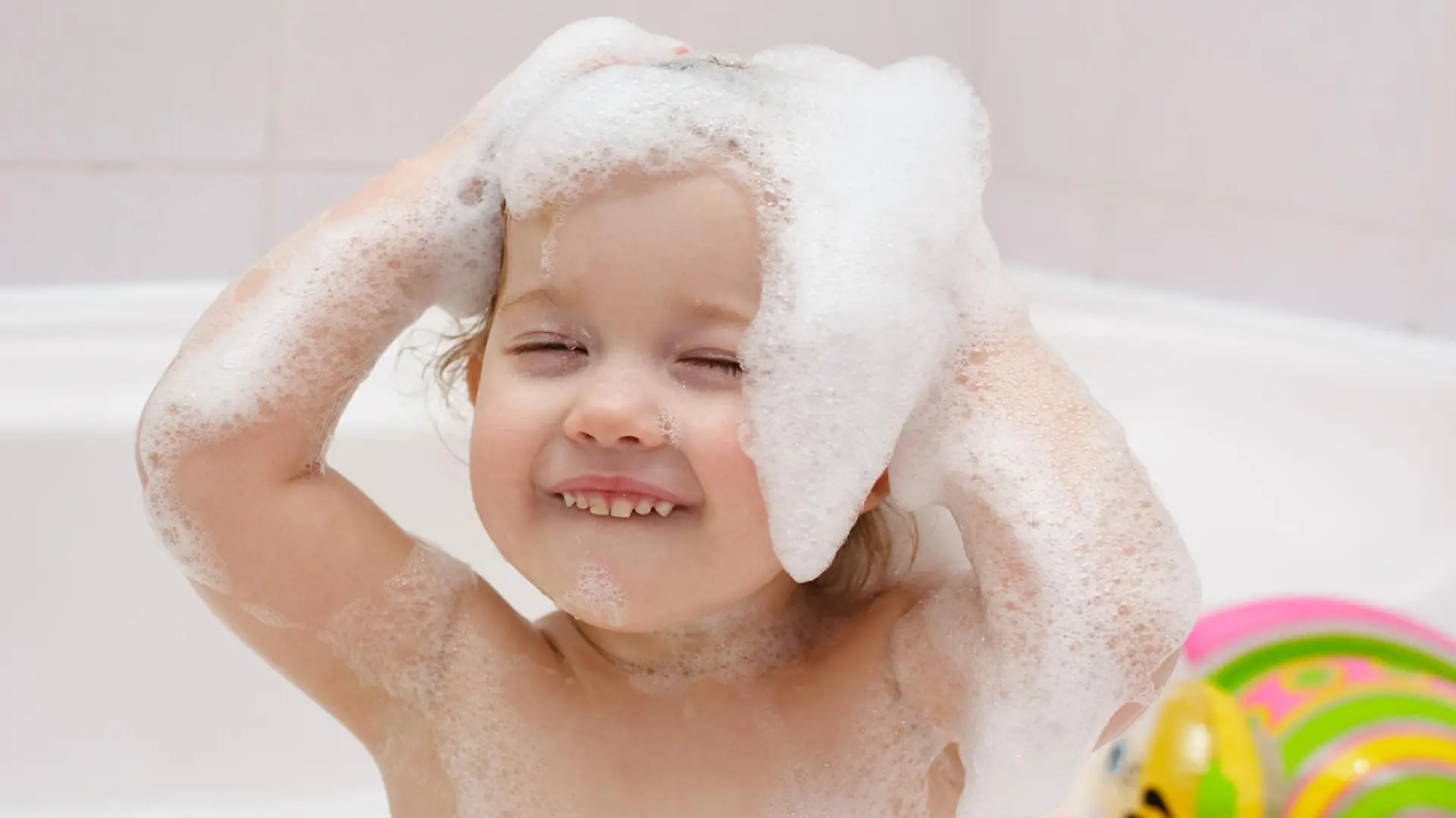 Cute baby is washing her hair in bath