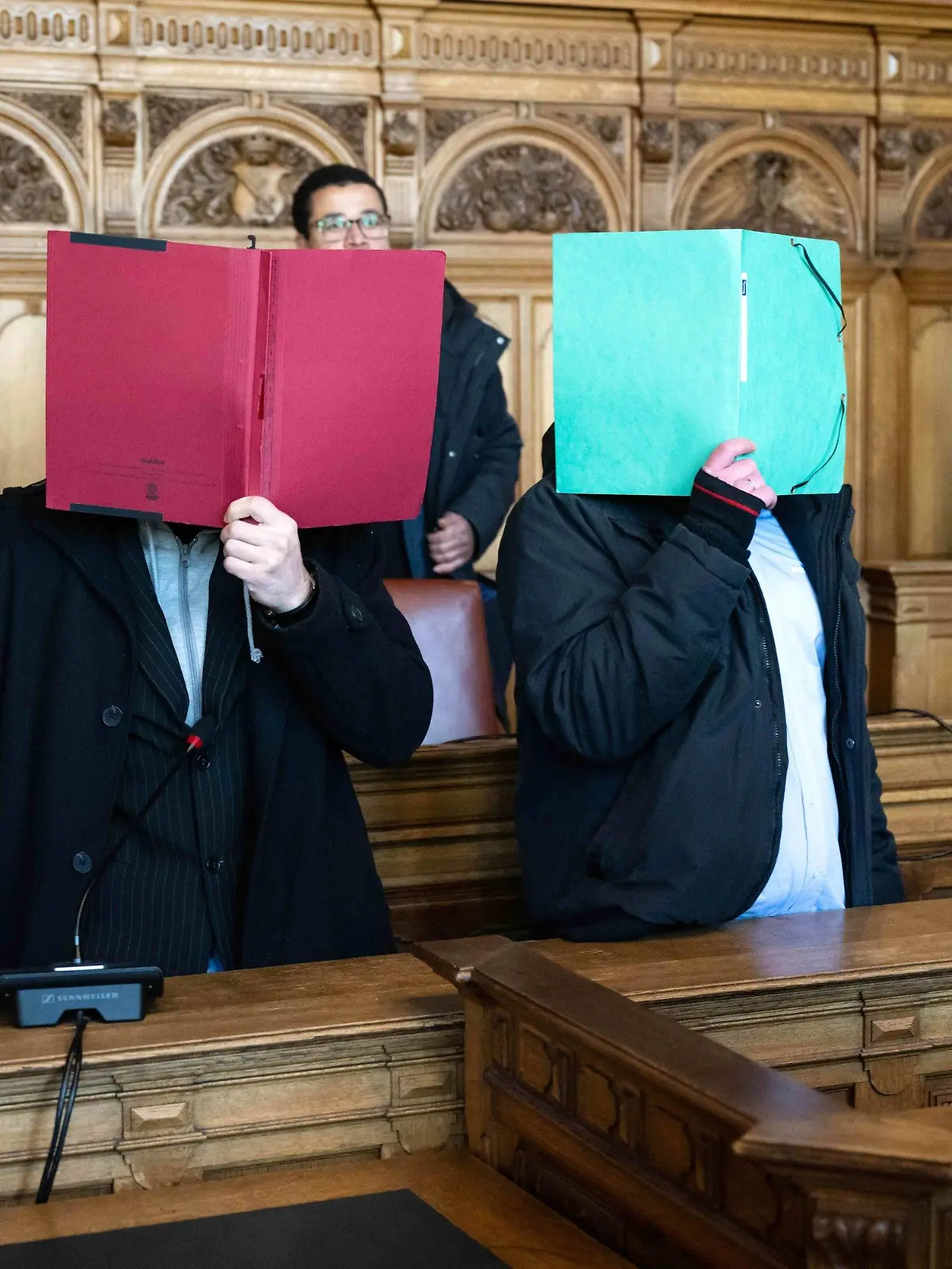08.02.2023, Bremen: Zwei Angeklagte stehen vor Prozessbeginn im Gerichtssaal und verbergen ihre Gesichter. Drei Männern wird vorgeworfen, im April 2020 einen Mann getötet zu haben. Foto: Sina Schuldt/dpa +++ dpa-Bildfunk +++