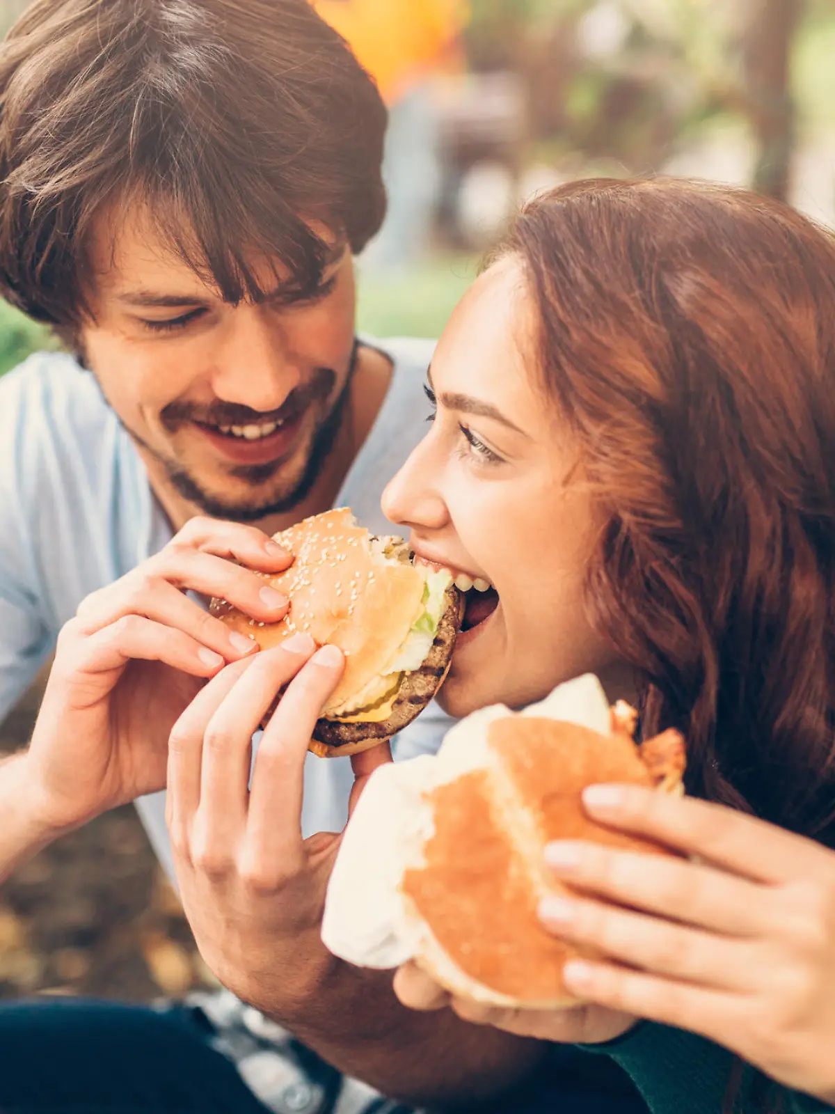 A man feeding his girlfriend a burger.