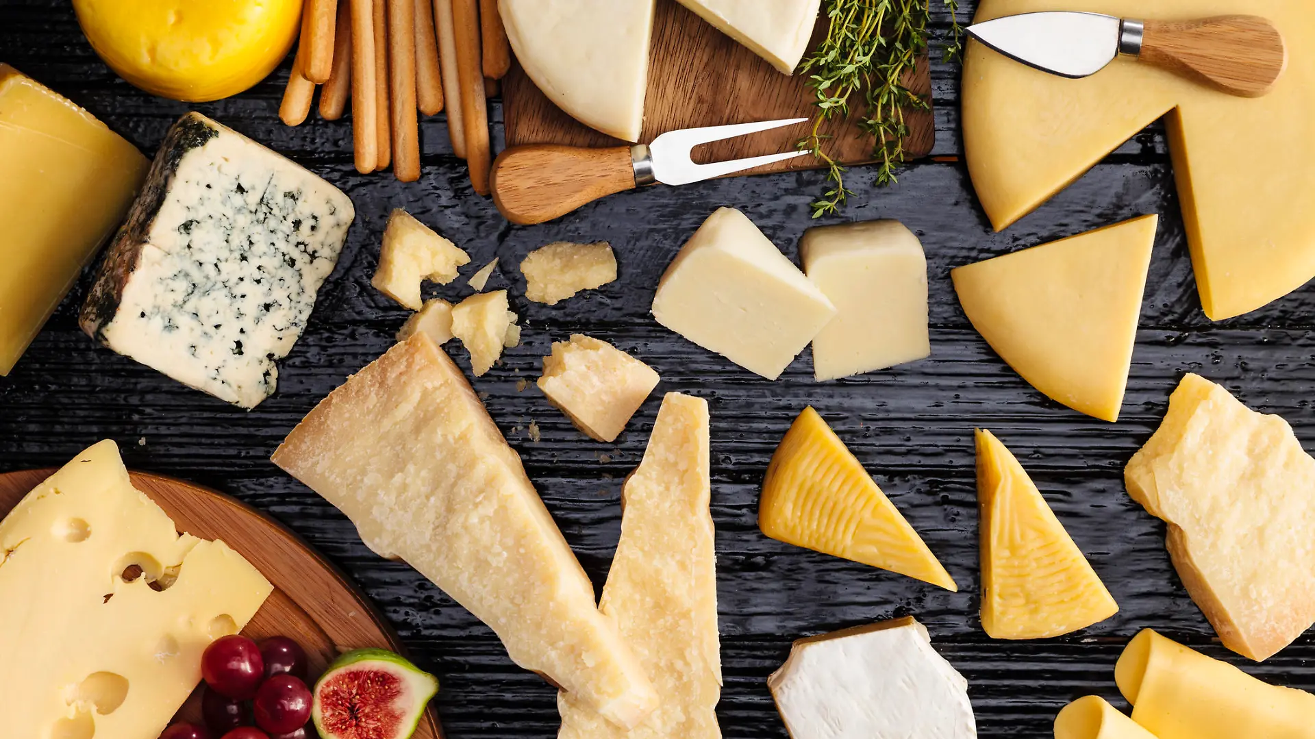 Top view of a dark table filled with a wide variety of cheeses.