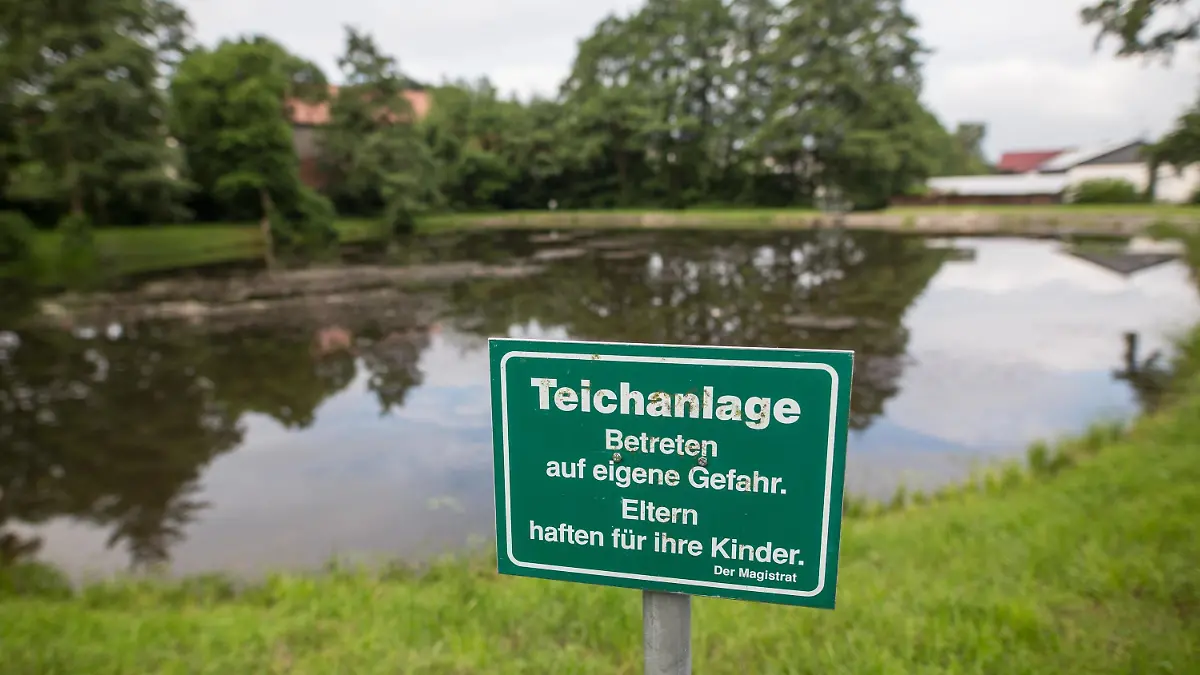 ARCHIV - 19.06.2016, Hessen, Neukirchen: Ein Schild mit der Aufschrift «Teichanlage - Betreten auf eigene Gefahr. Eltern haften für ihre Kinder.» steht an einem Teich im Ortsteil Seigertshausen. Nachdem drei Kinder in dem Dorfteich ertrunken waren, wurde der Bürgermeister wegen fahrlässiger Tötung angeklagt. (zu dpa «Bürgermeister wegen Tod von drei ertrunkenen Geschwistern angeklagt» vom 23.02.2018) Foto: Frank Rumpenhorst/dpa +++ dpa-Bildfunk +++