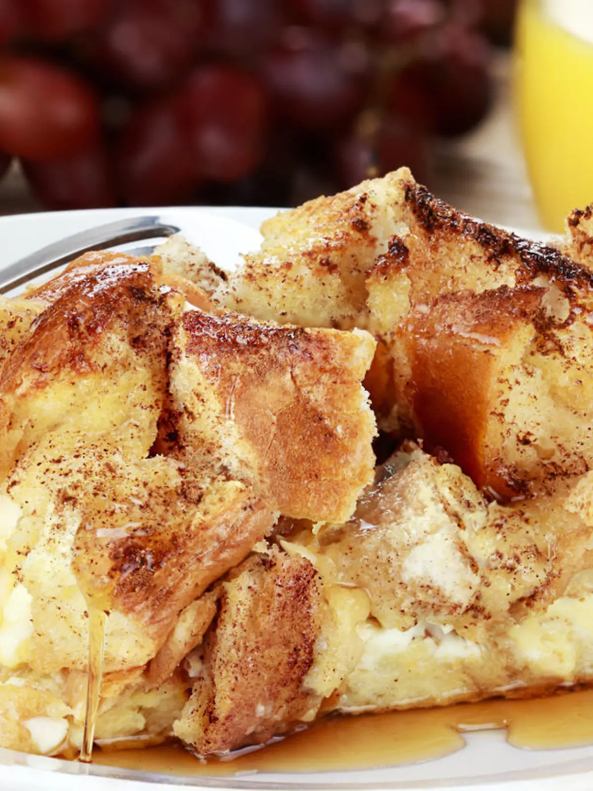 French toast casserole with maple syrup. Made with cream cheese cheese in the center. Fresh grapes and orange juice in background.