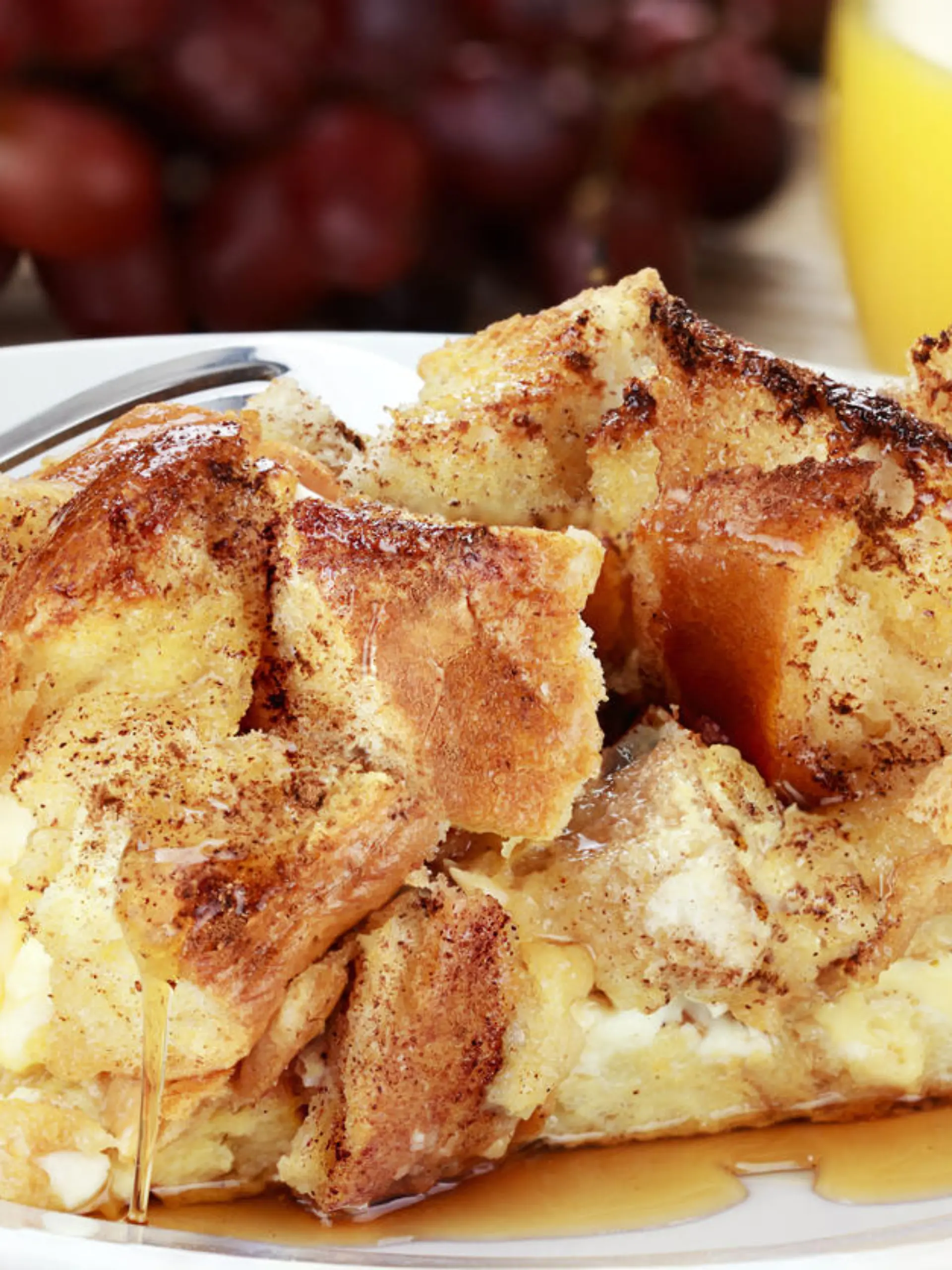 French toast casserole with maple syrup. Made with cream cheese cheese in the center. Fresh grapes and orange juice in background.