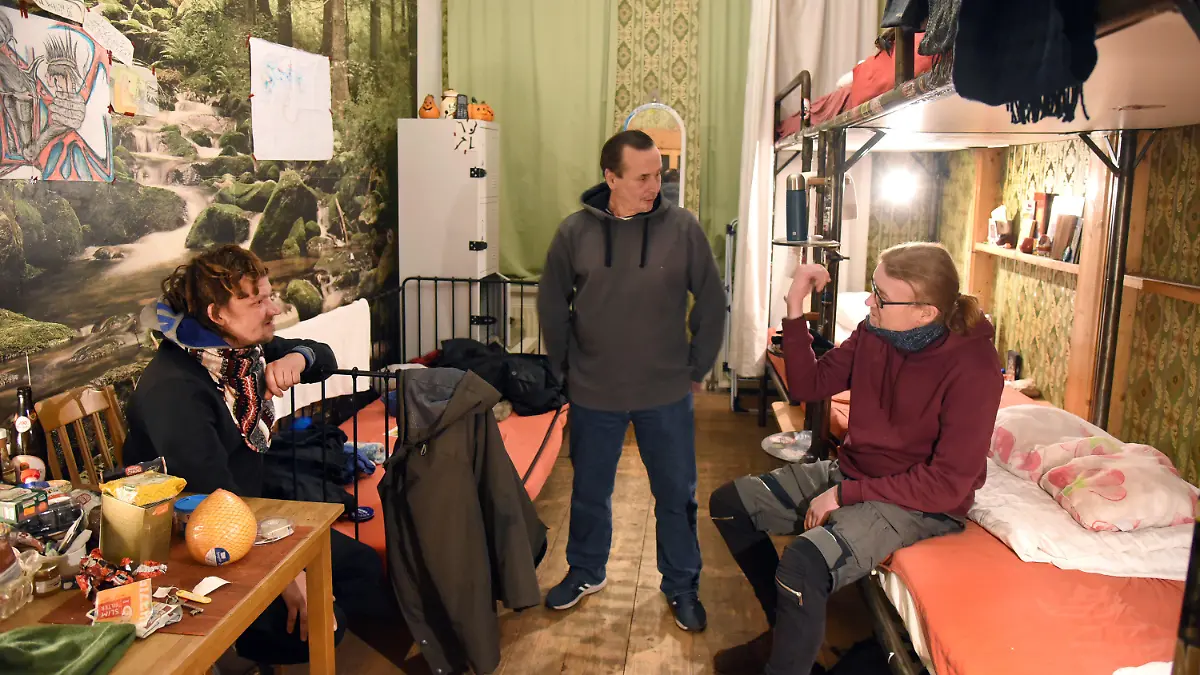 PRODUKTION - 24.01.2023, Sachsen, Leipzig: Im HomePlanet Hostel im Stadtteil Connewitz besucht der im vorigen Jahr noch obdachlose 51-jährige Ralf Mertes (M) die zwei Obdachlosen, den 39-jährigen Michael Schönrock (l) und den 50-jährigen Wladimir in ihrem Zimmer. Das Hostel stellt eine Etage für wohnungslose Menschen zur Verfügung, kostenlos - mit Frühstück und Abendbrot.     (zu dpa "«Erinnert an Urlaub» - Hostel in Leipzig nimmt Obdachlose auf") Foto: Waltraud Grubitzsch/dpa +++ dpa-Bildfunk +++