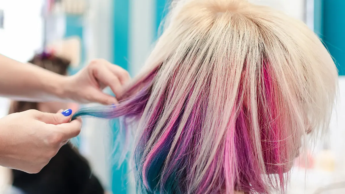 Hairdresser holding cowlick of client colored hair and making haircut in beauty salon. Fresh colored rainbow hair.