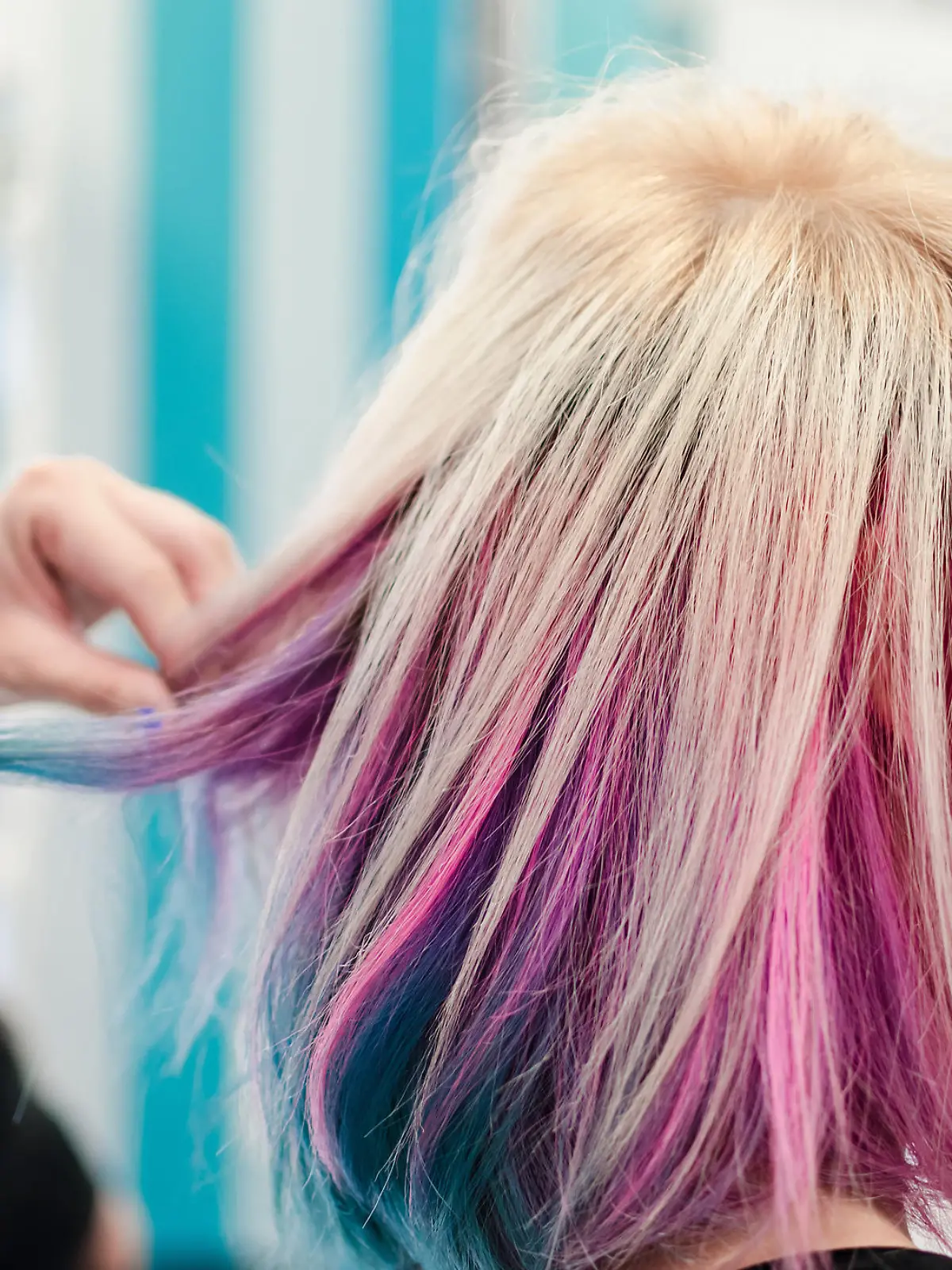 Hairdresser holding cowlick of client colored hair and making haircut in beauty salon. Fresh colored rainbow hair.