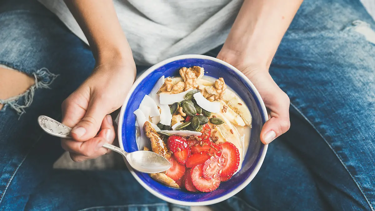Eating healthy breakfast bowl. Yogurt, granola, seeds, fresh and dry fruits and honey in blue ceramic bowl in woman' s hands. Clean eating, dieting, detox, vegetarian food concept