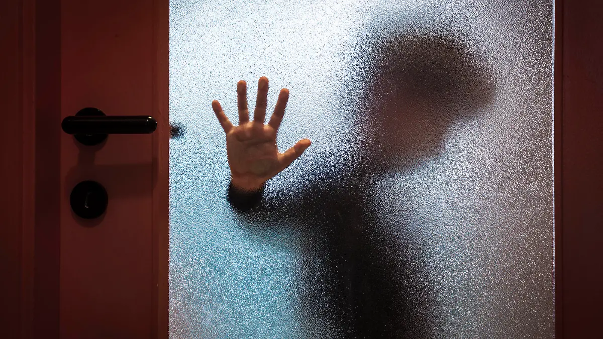 Blurred sad boy leaning open hand against glass door.