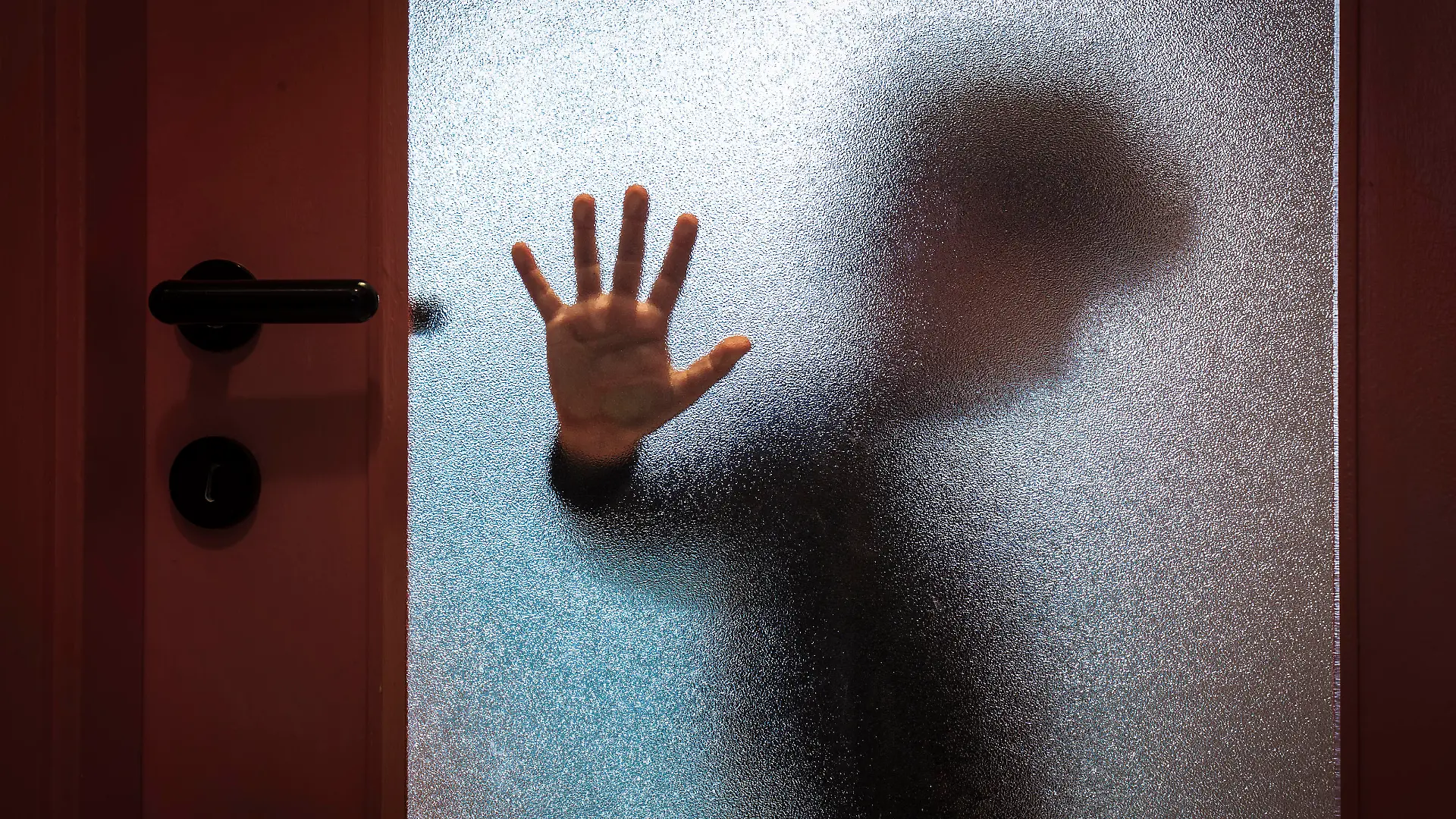 Blurred sad boy leaning open hand against glass door.