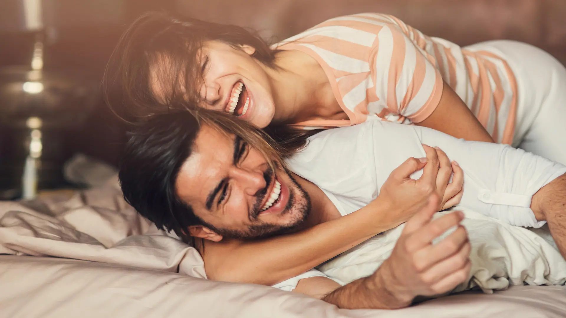 Happy young playful couple in bed.