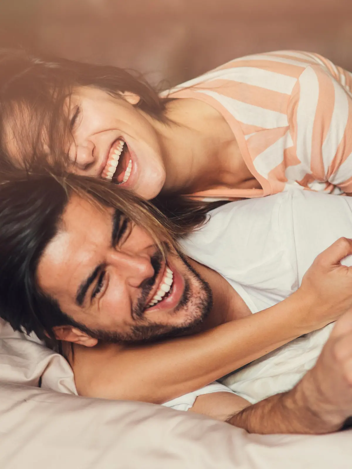 Happy young playful couple in bed.