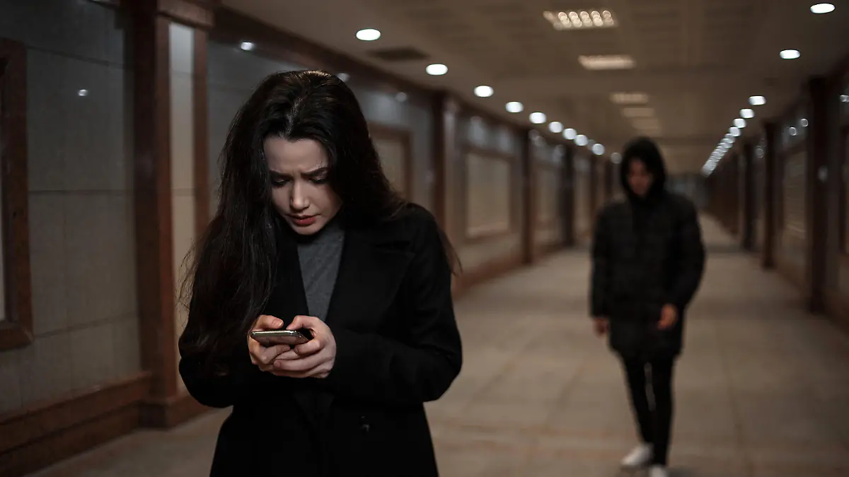 a young beautiful woman walks through an underground passage at night, followed by a man in dark clothing with a hood on his head. a woman tries to dial the number of the rescue service on the phone