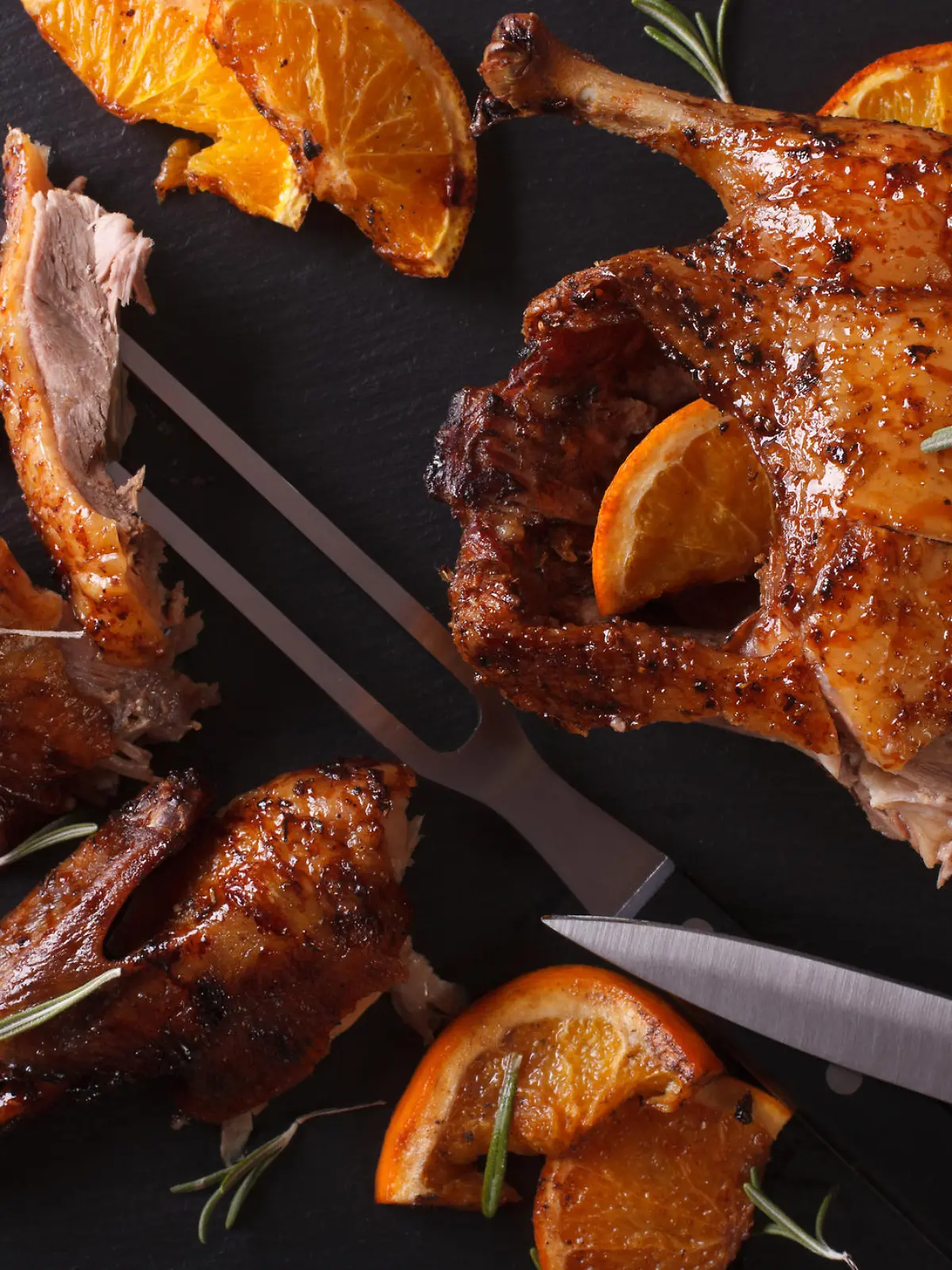 Cutting the roast duck and oranges closeup on a black slate board. horizontal view from above