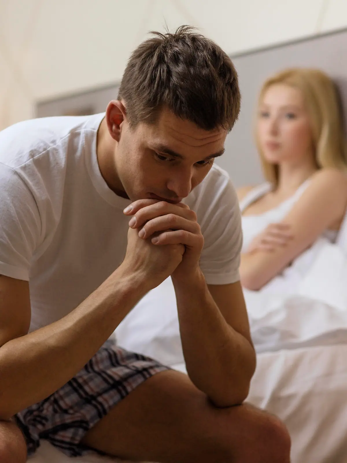 hotel, travel, relationships, and sexual problems concept - upset man sitting on the bed with woman on the back