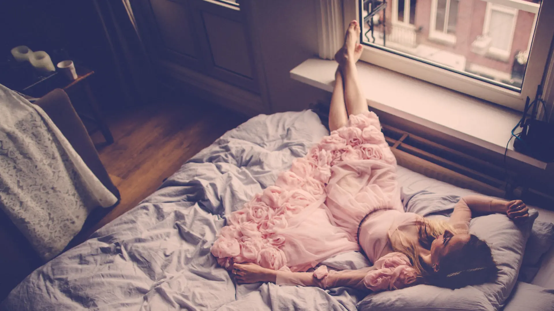 Portrait of a beautiful woman, resting on the bed by the window in a beautiful pink dress