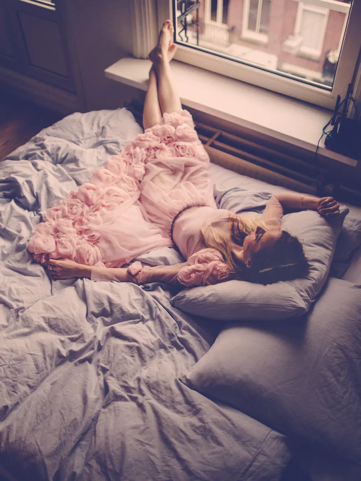 Portrait of a beautiful woman, resting on the bed by the window in a beautiful pink dress 