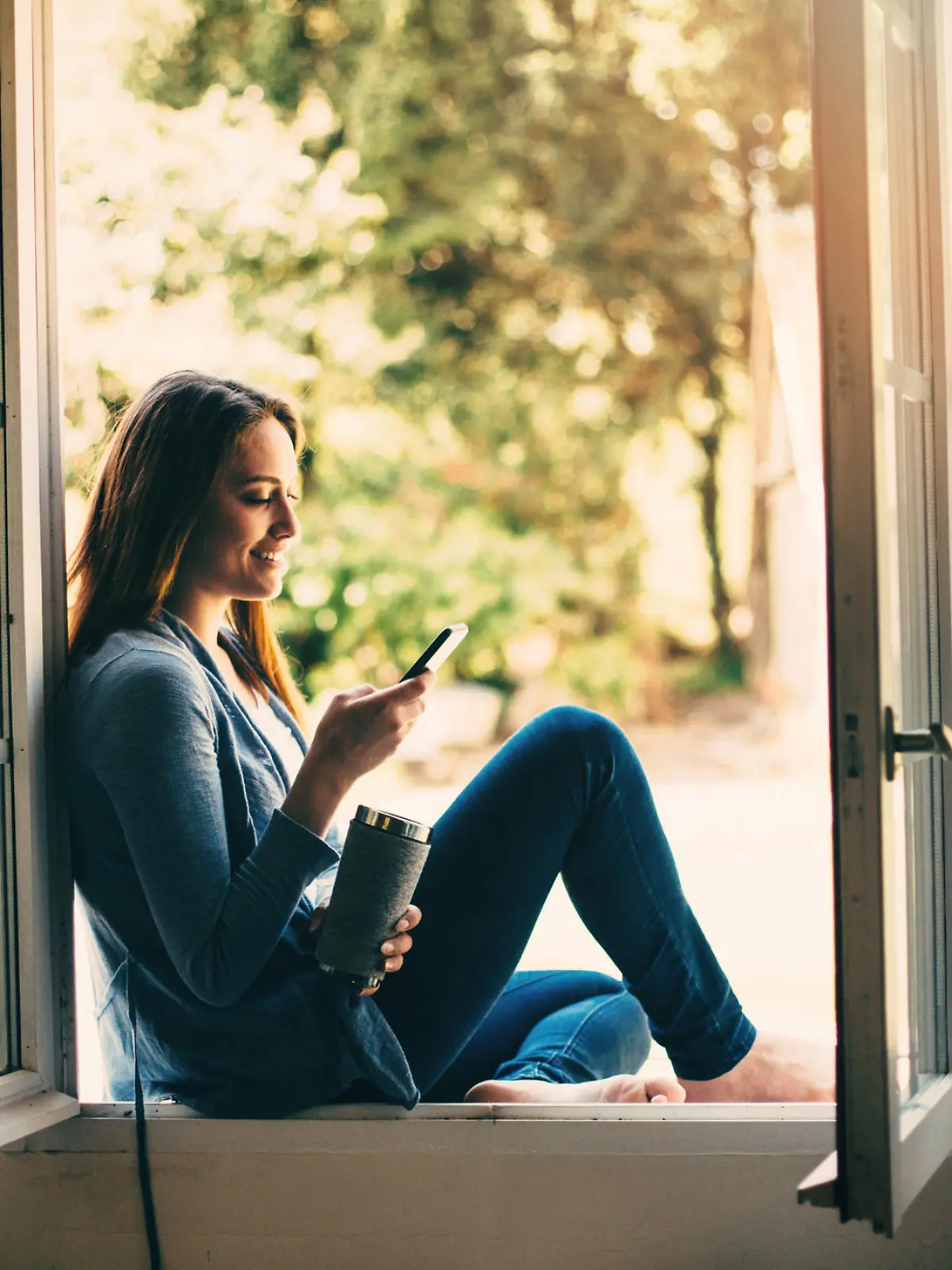 Beautiful young woman holding a cup of coffee an texting at home