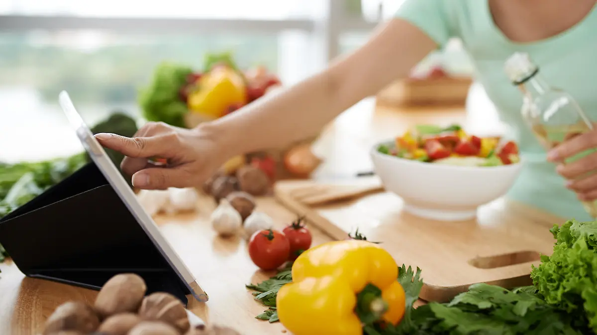 Woman checking recipe on digital tablet before seasoning salad