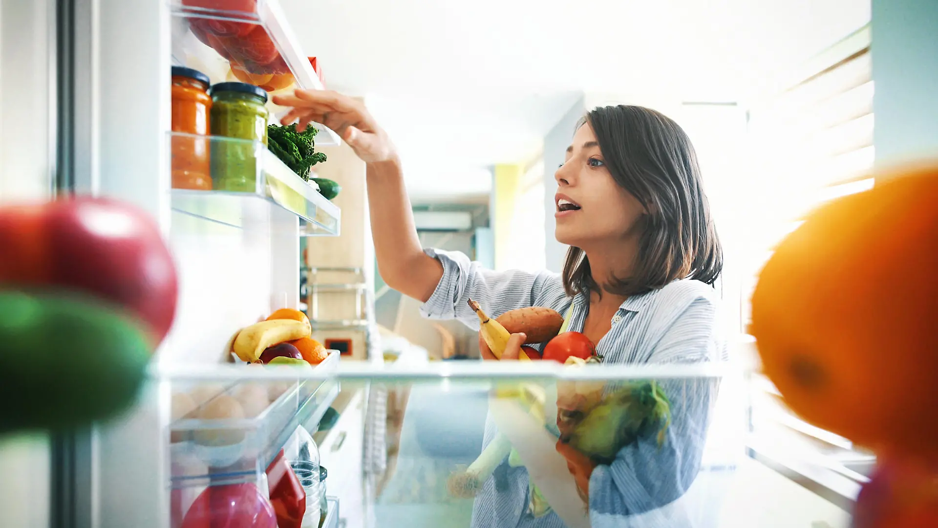 Closeup of a cheerful young couple picking some fruit and veggies from the fridge to make some healthy breakfast on Sunday morning. Shot from inside the working fridge.