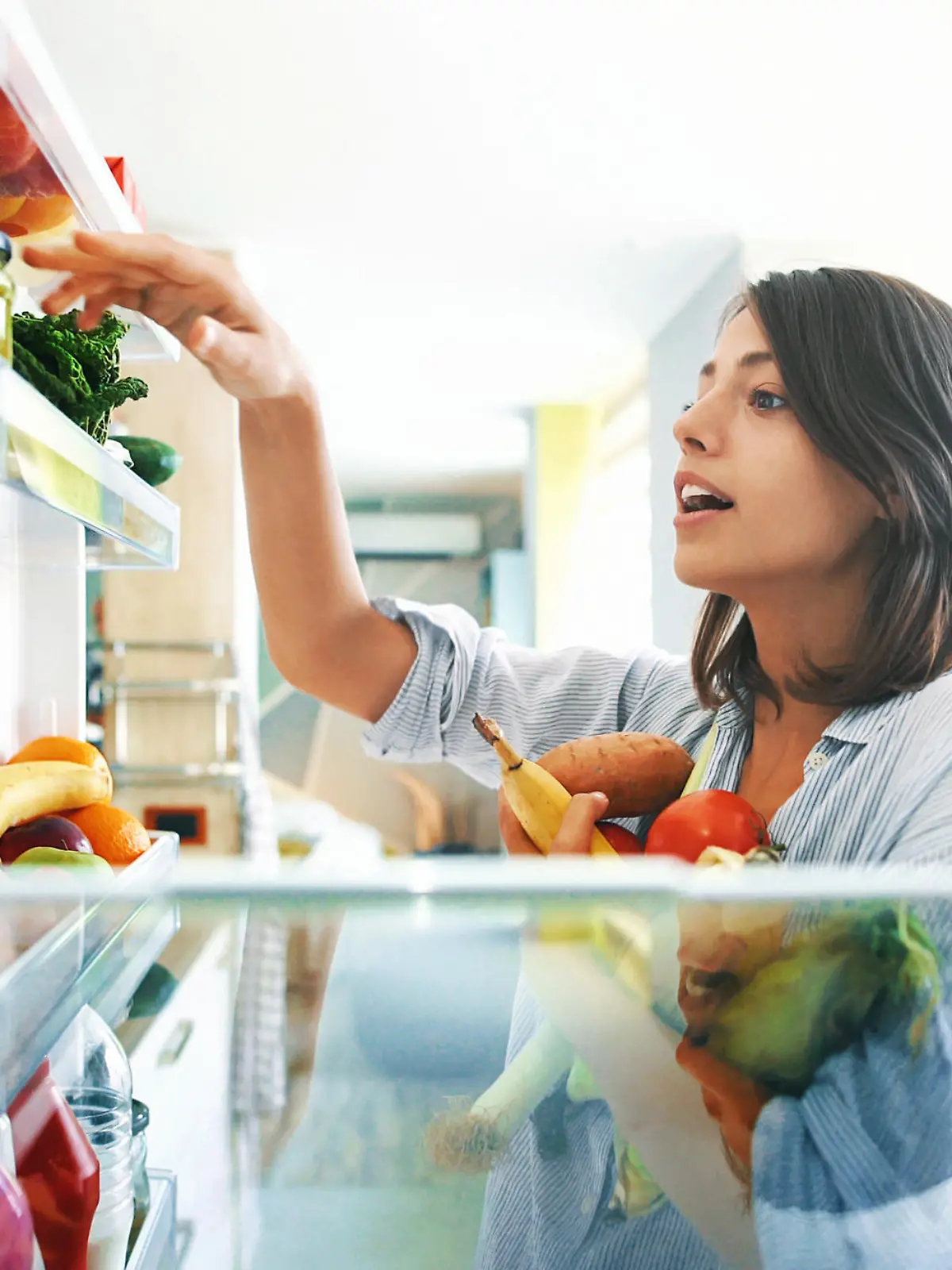 Closeup of a cheerful young couple picking some fruit and veggies from the fridge to make some healthy breakfast on Sunday morning. Shot from inside the working fridge.