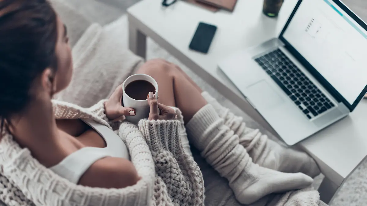 Top view of attractive young woman holding cup while relaxing on couch at home