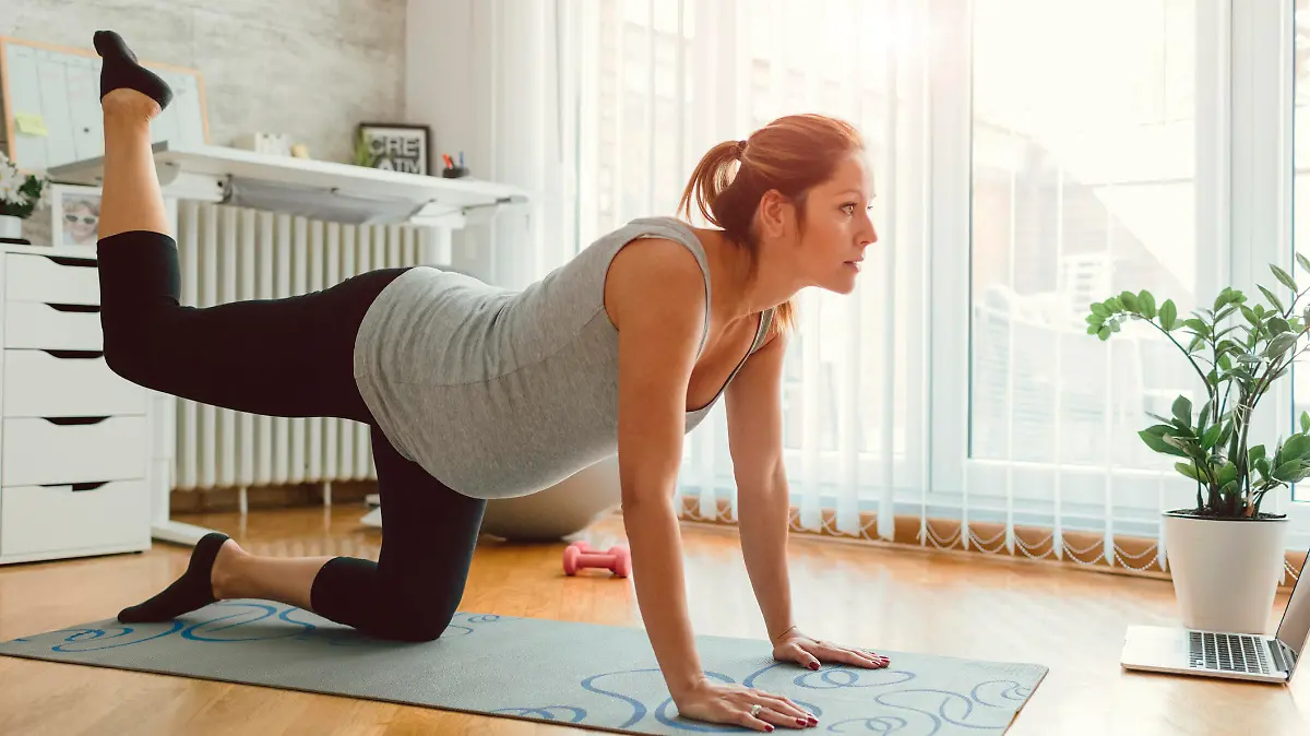 30 weeks pregnant woman exercising at home. Exercising on exercise mat and working stretching exercise.