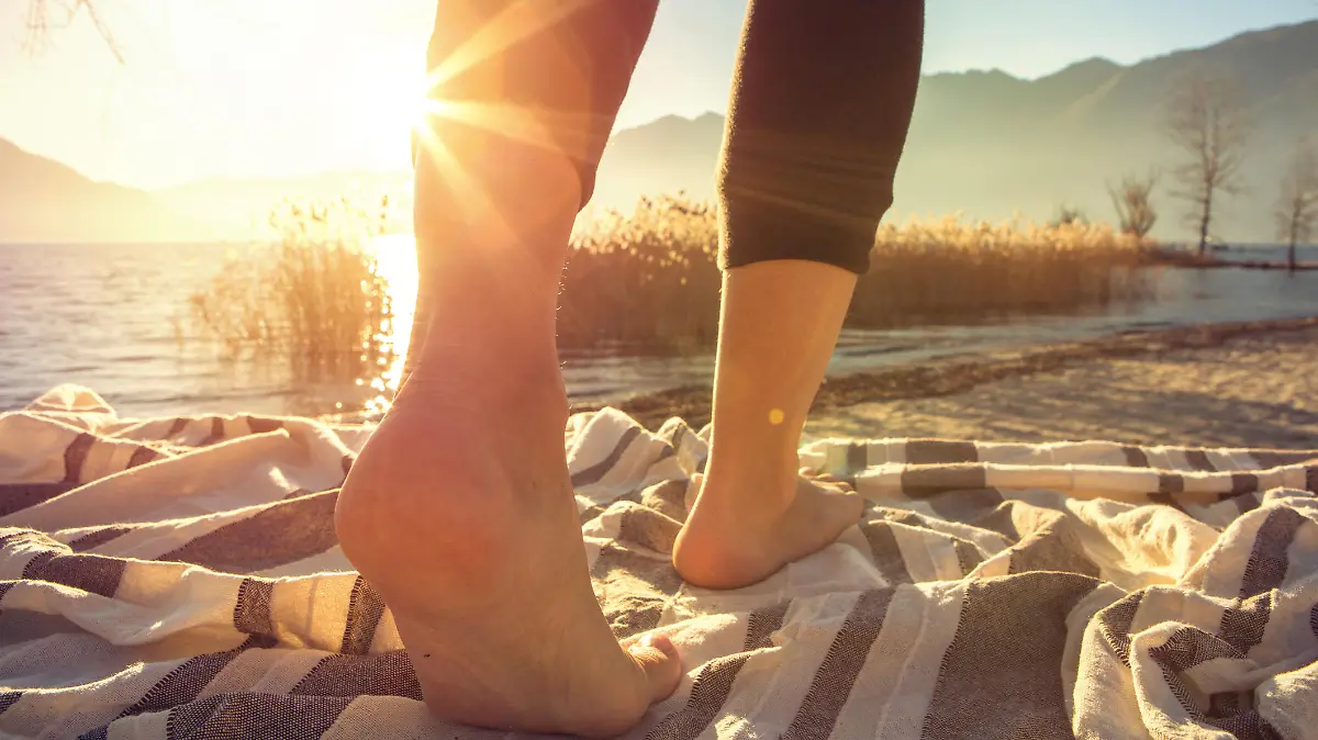 Close up on woman's feet standing on a boat above the lake, sunbeam on the skin.