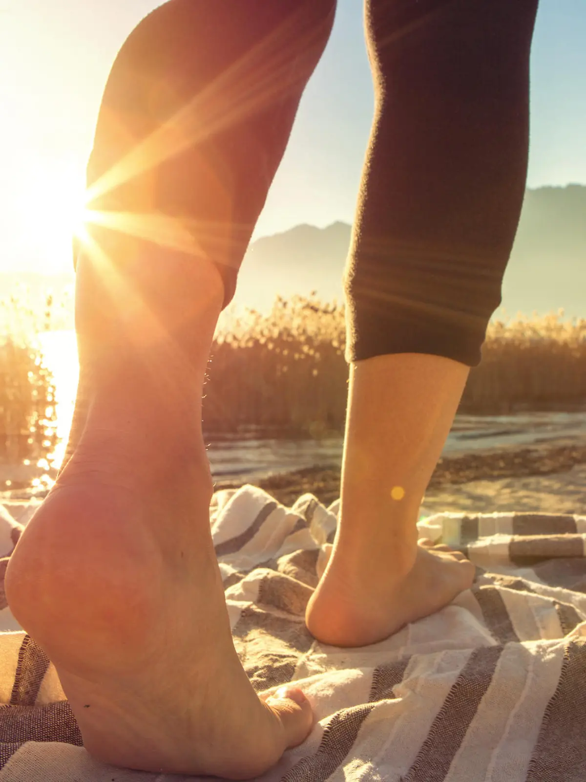 Close up on woman's feet standing on a boat above the lake, sunbeam on the skin.