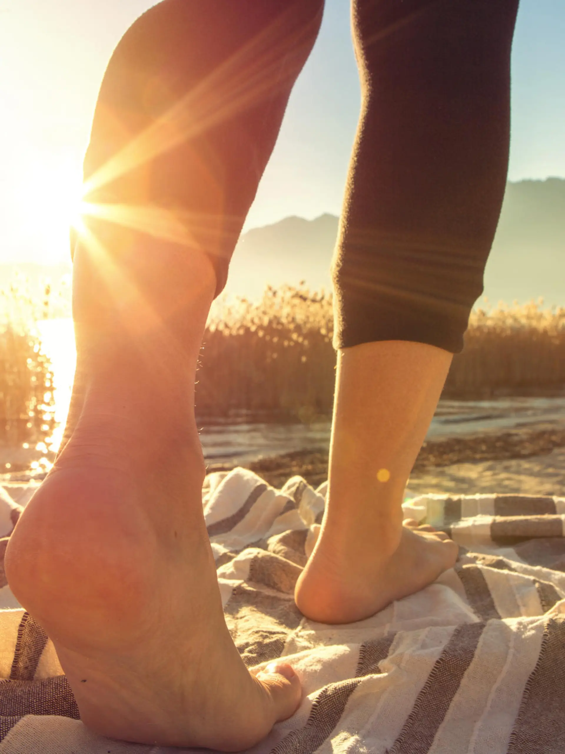 Close up on woman's feet standing on a boat above the lake, sunbeam on the skin.