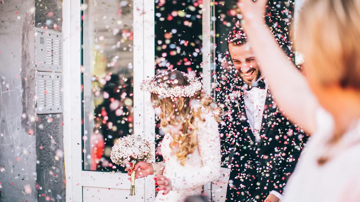 Photo of just married couple. Guests are throwing confetti in the air.