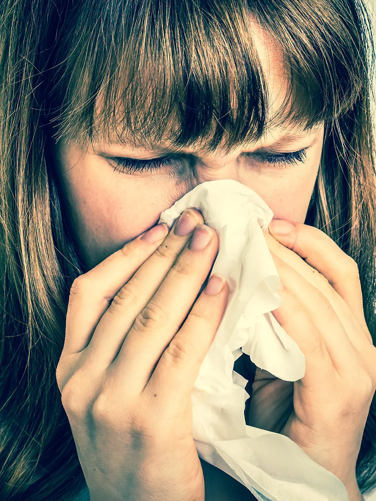 Young woman with allergy or flu cold symptoms sneezing in tissue