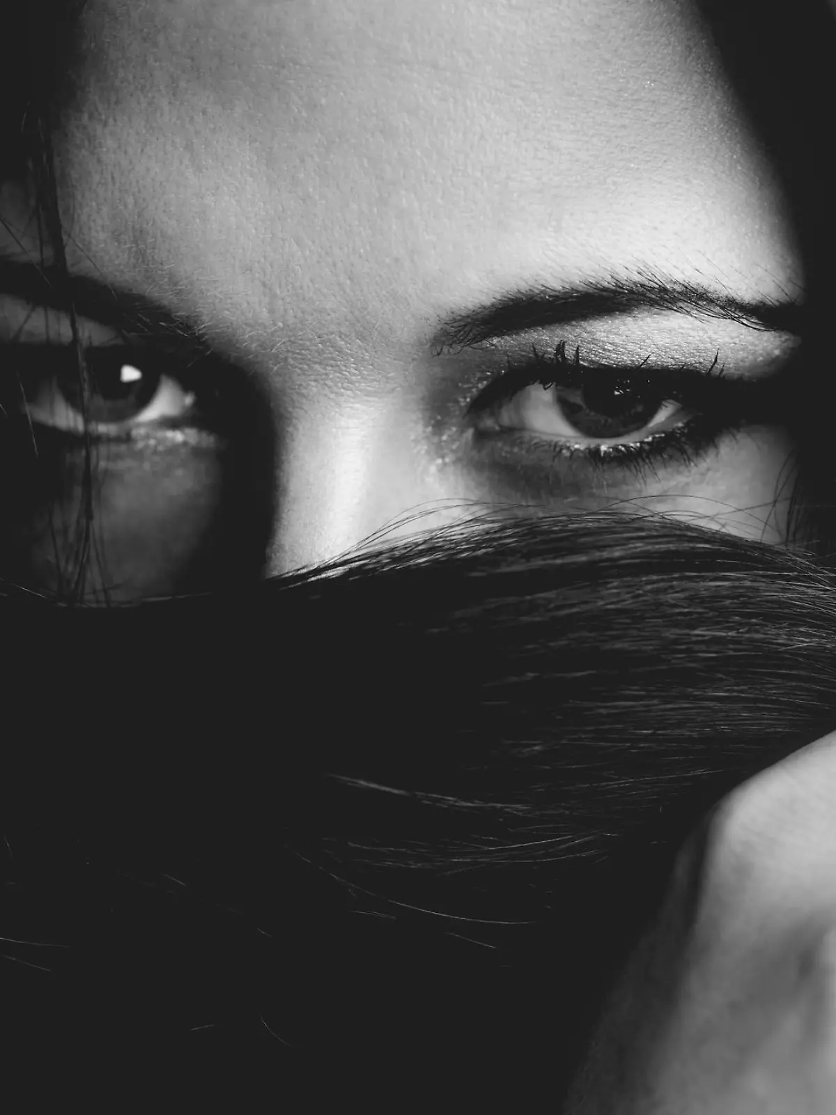 Cropped monochrome portrait of a beautiful young woman covering her mouth with her hair