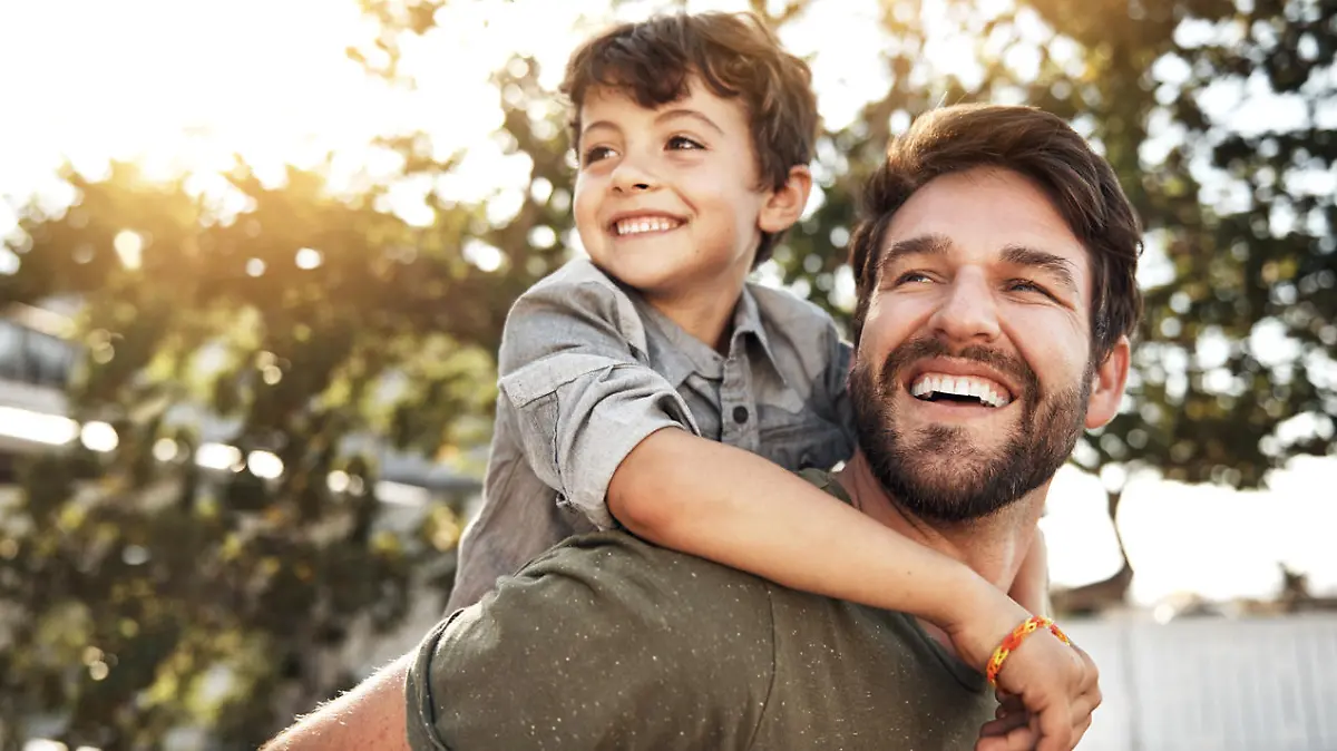 Portrait of a happy father giving his little boy a piggyback ride in their backyard