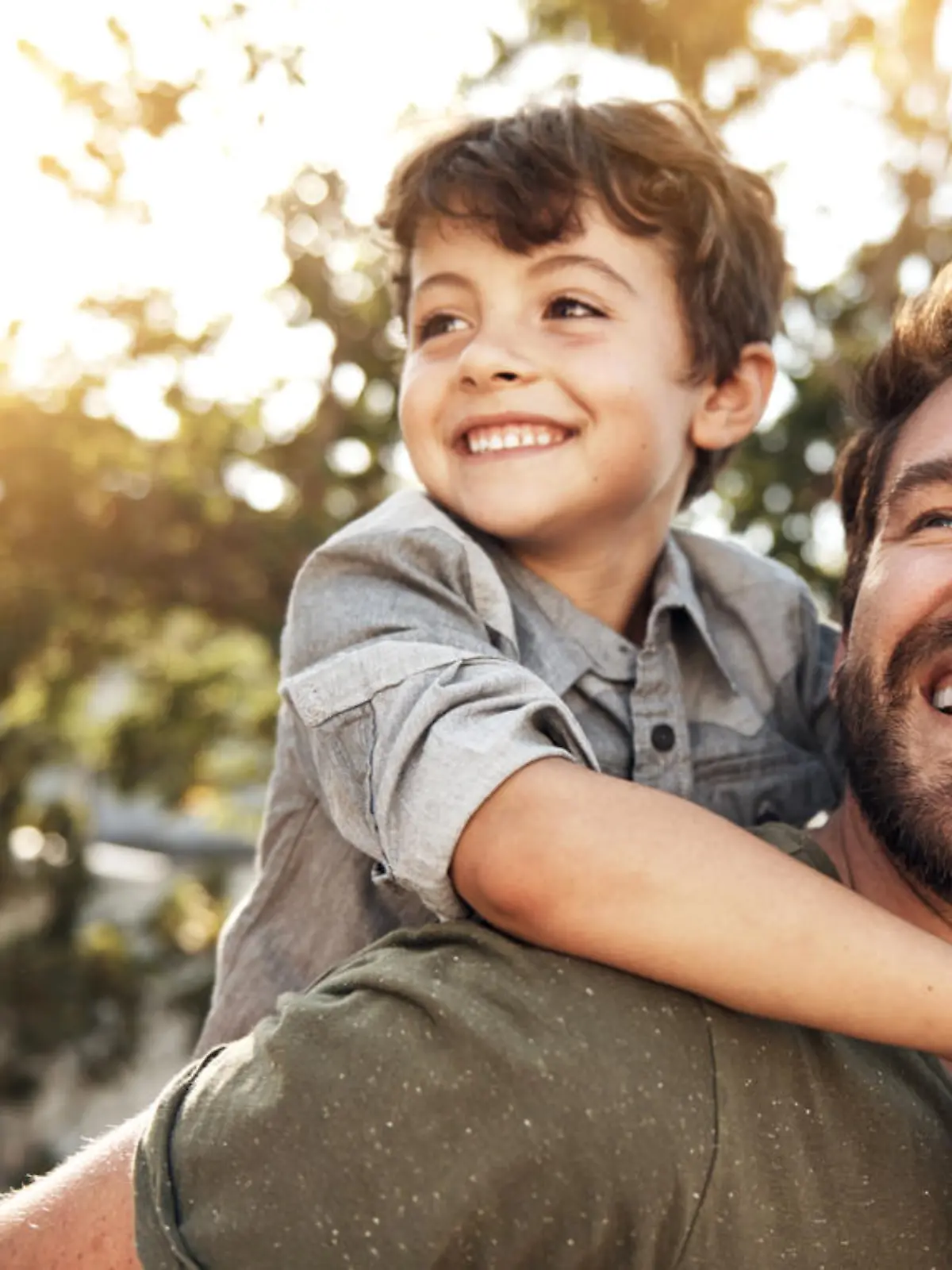 Portrait of a happy father giving his little boy a piggyback ride in their backyard