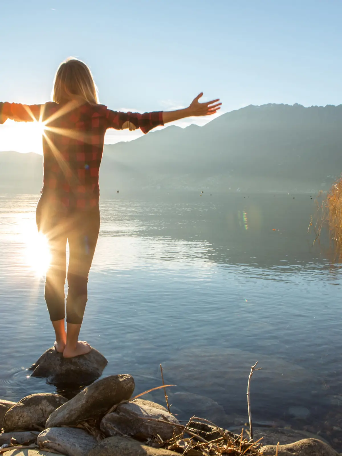 Young cheerful woman by the lake enjoying nature. Arms outstretched for positive emotion. 