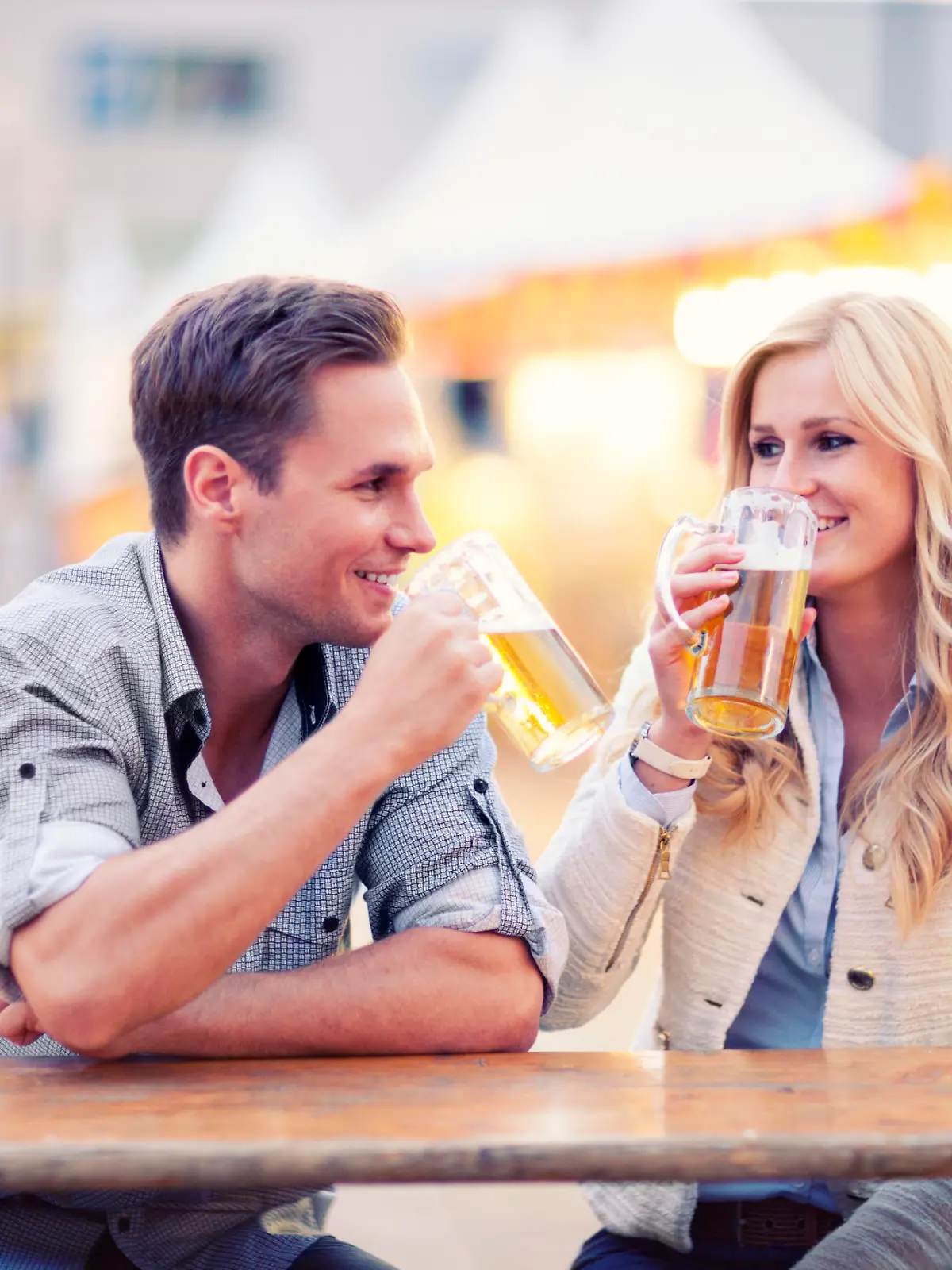 A young happy couple is sitting at a table and drinking beer during the traditional festival on the Alexanderplatz (Eastern Berlin, Germany) late in the evening.