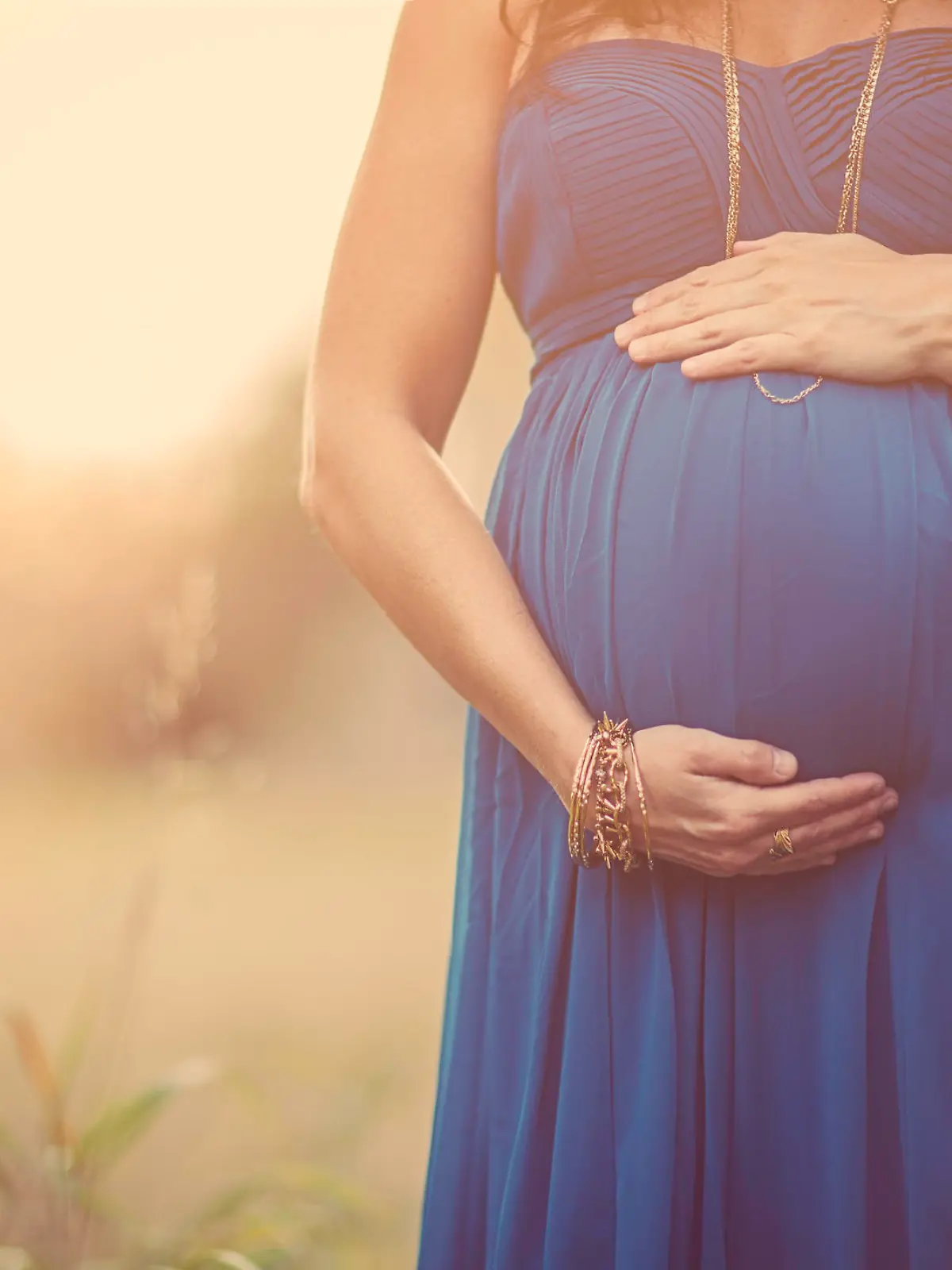 Portrait of a beautiful pregnant woman (7months) wearing a long teal dress standing within a Autumn setting. Details of mother holding her belly.
