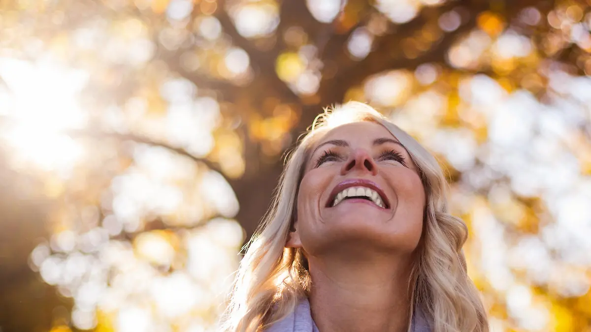 Smiling woman looking up against trees at park during autumn